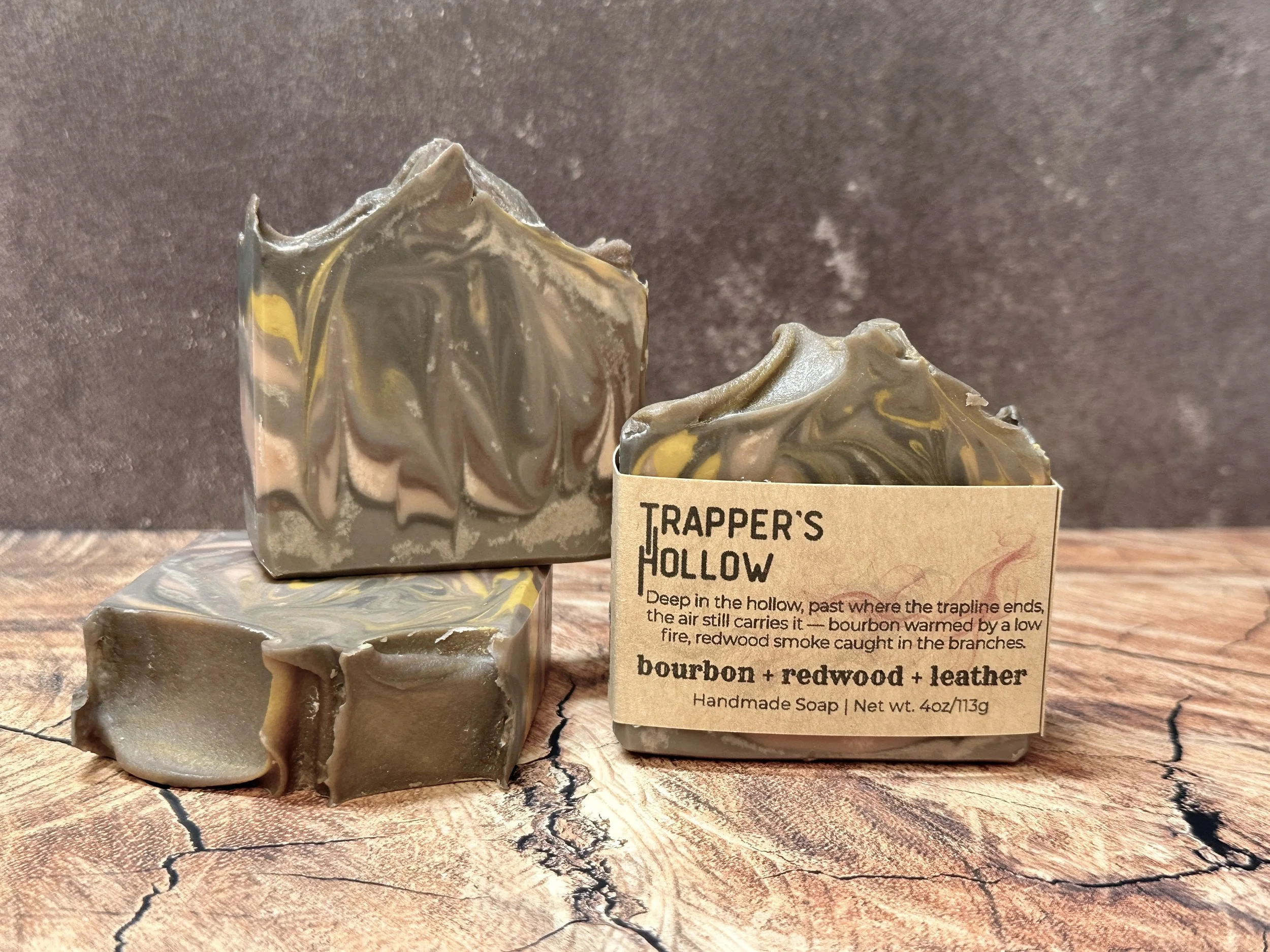 Photo of handcrafted artisan soaps, posed to appeal. One soap shows a label with the soap's name, Trapper's Hollow. The soaps made of swirls of brown, with additions of yellow and peach.