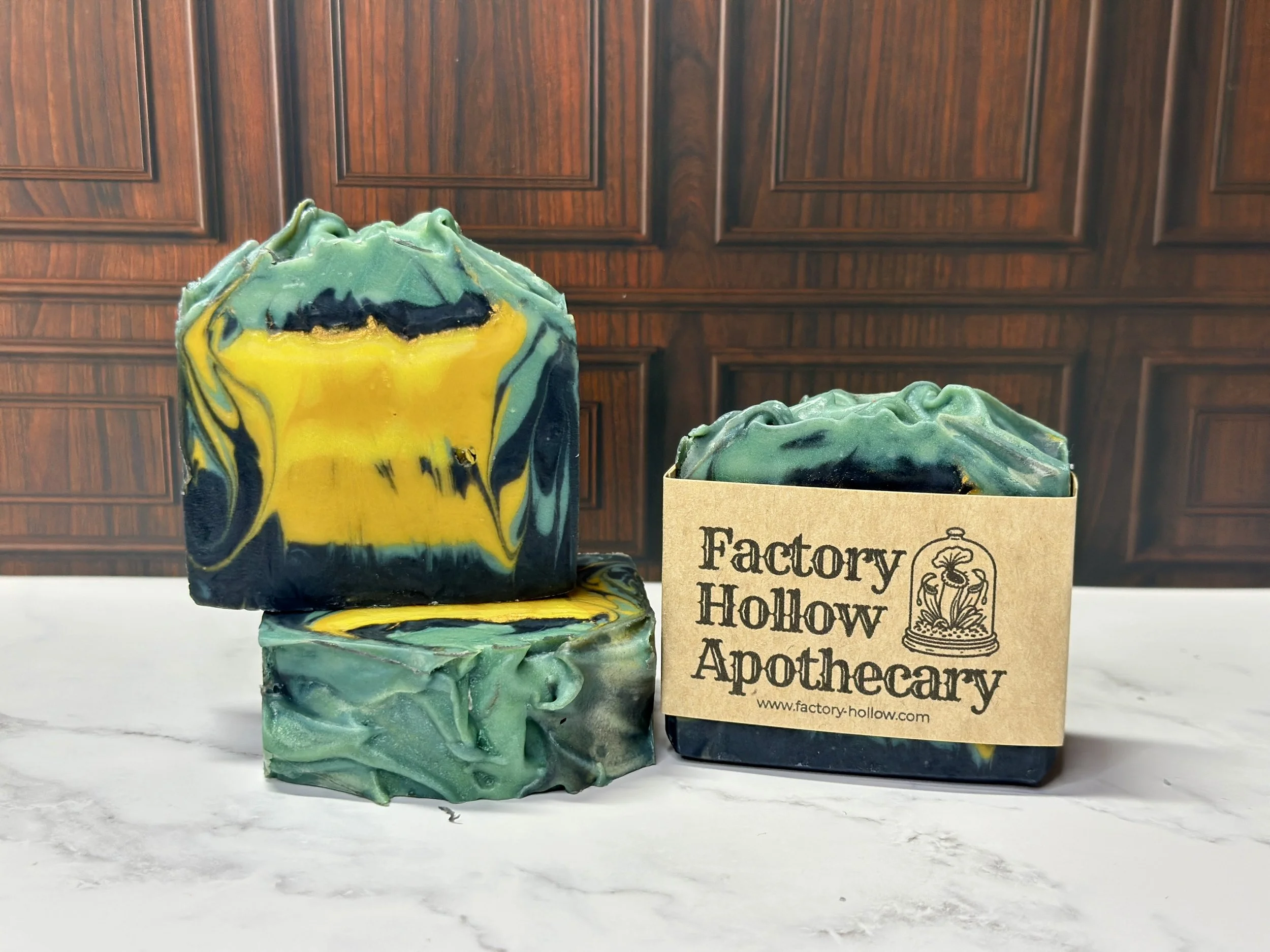 Photo of handcrafted artisan soaps, posed to appeal. One soap shows a label with the maker's name, Factory Hollow Apothecary. The soaps include bright and muted yellows, teal, and deep blue.