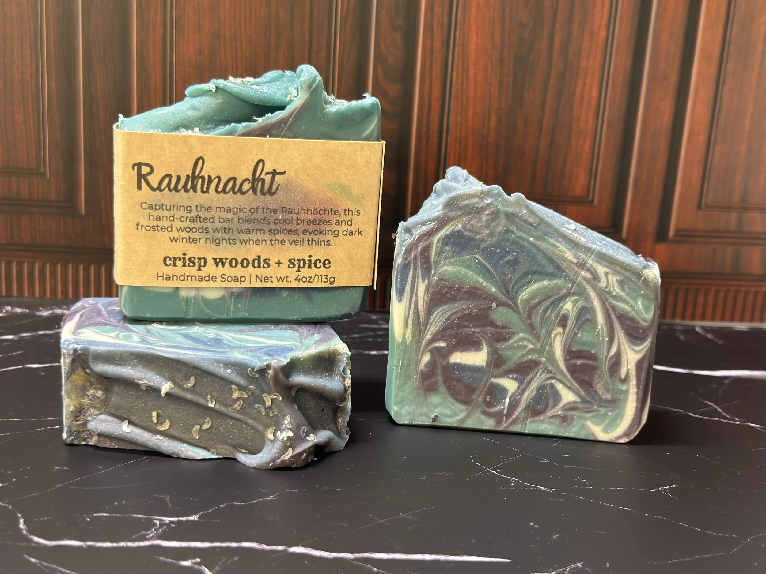 Photo of handcrafted artisan soaps, posed to appeal. The soaps are made of deep blue, teal, purple, and lighter blue swirls, topped with biodegradable glitter.