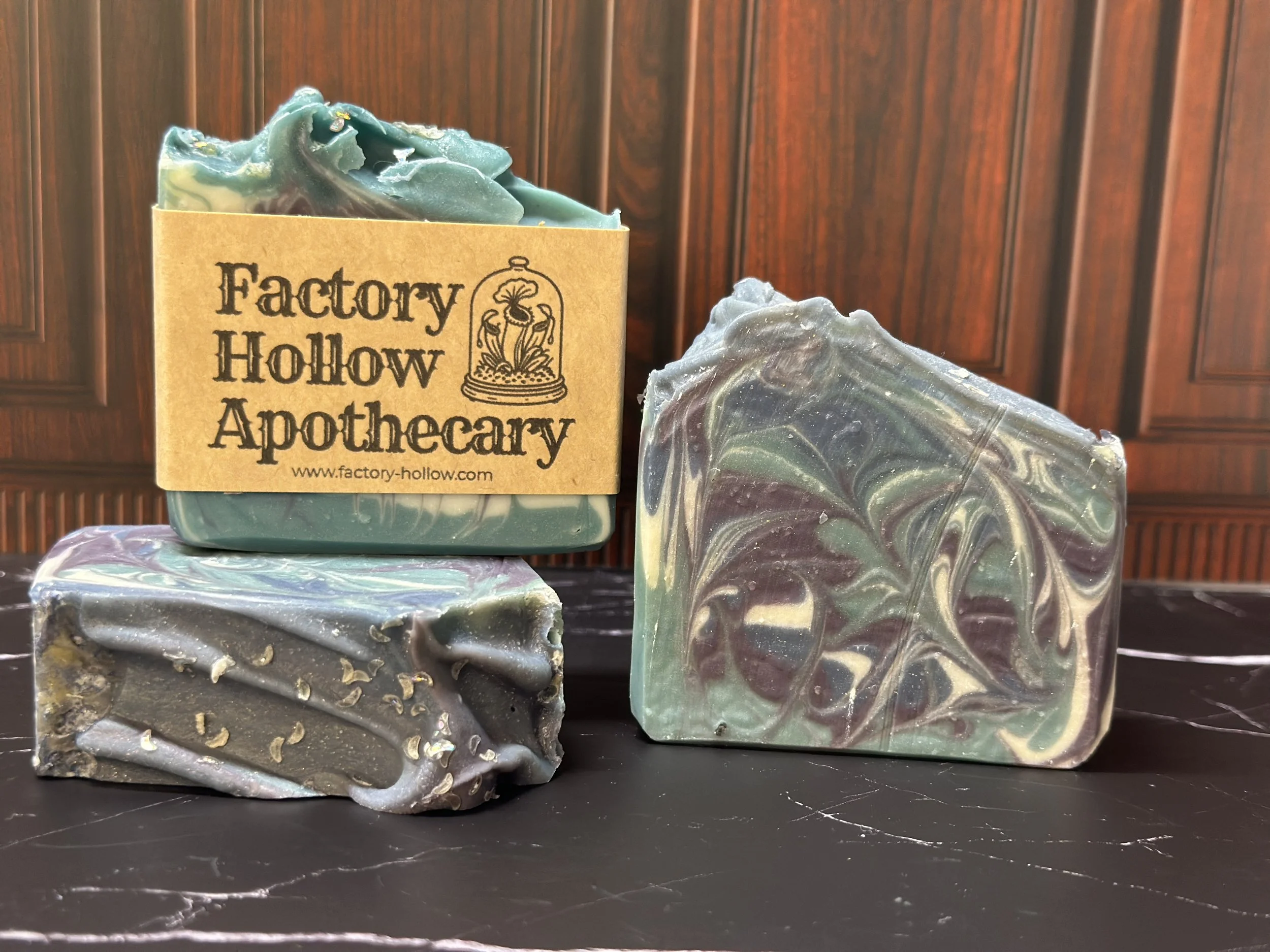 Photo of handcrafted artisan soaps, posed to appeal. The soaps are made of deep blue, teal, purple, and lighter blue swirls, topped with biodegradable glitter.