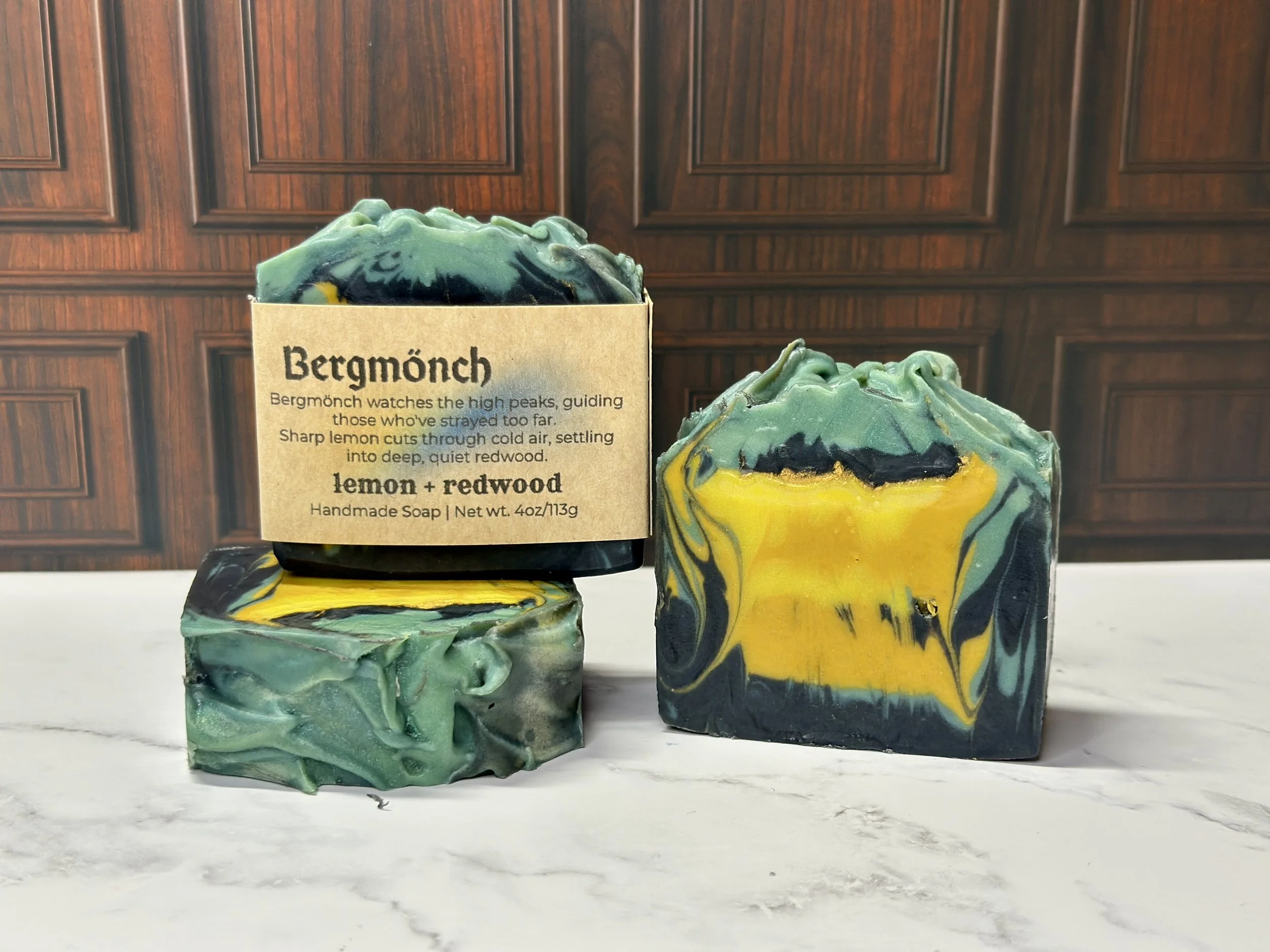 Photo of handcrafted artisan soaps, posed to appeal. One soap shows a label with the soap's name, Bergmönch. The soaps include bright and muted yellows, teal, and deep blue.
