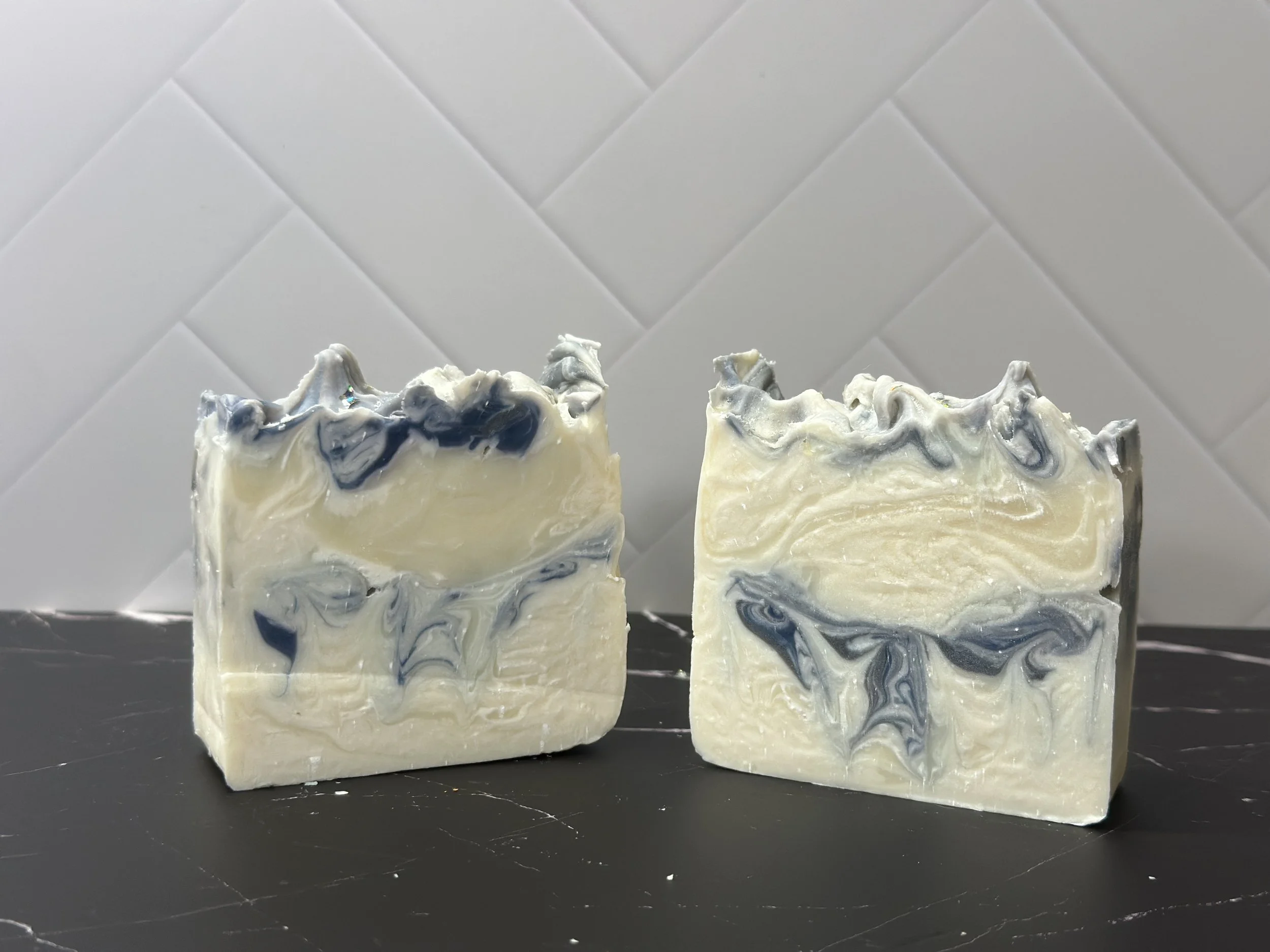 Photo of handcrafted artisan soaps, posed to appeal. The soaps are primarily a bright, icy white with threads of deep blue and a tinge of lilac.