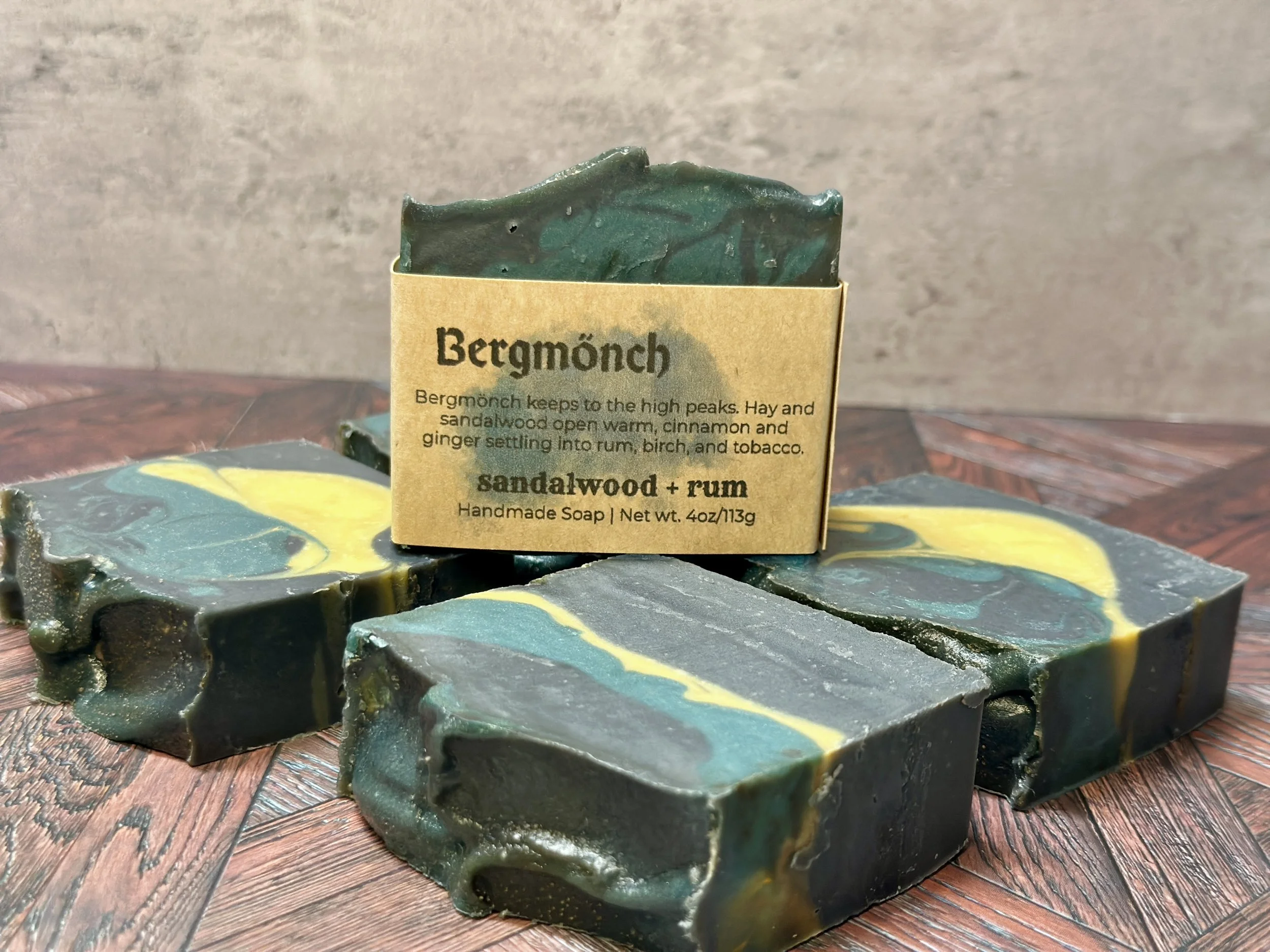 Photo of handcrafted artisan soaps, posed to appeal. One soap shows a label with the soap's name, Bergmönch. The soaps include bright and muted yellows, teal, and deep blue.
