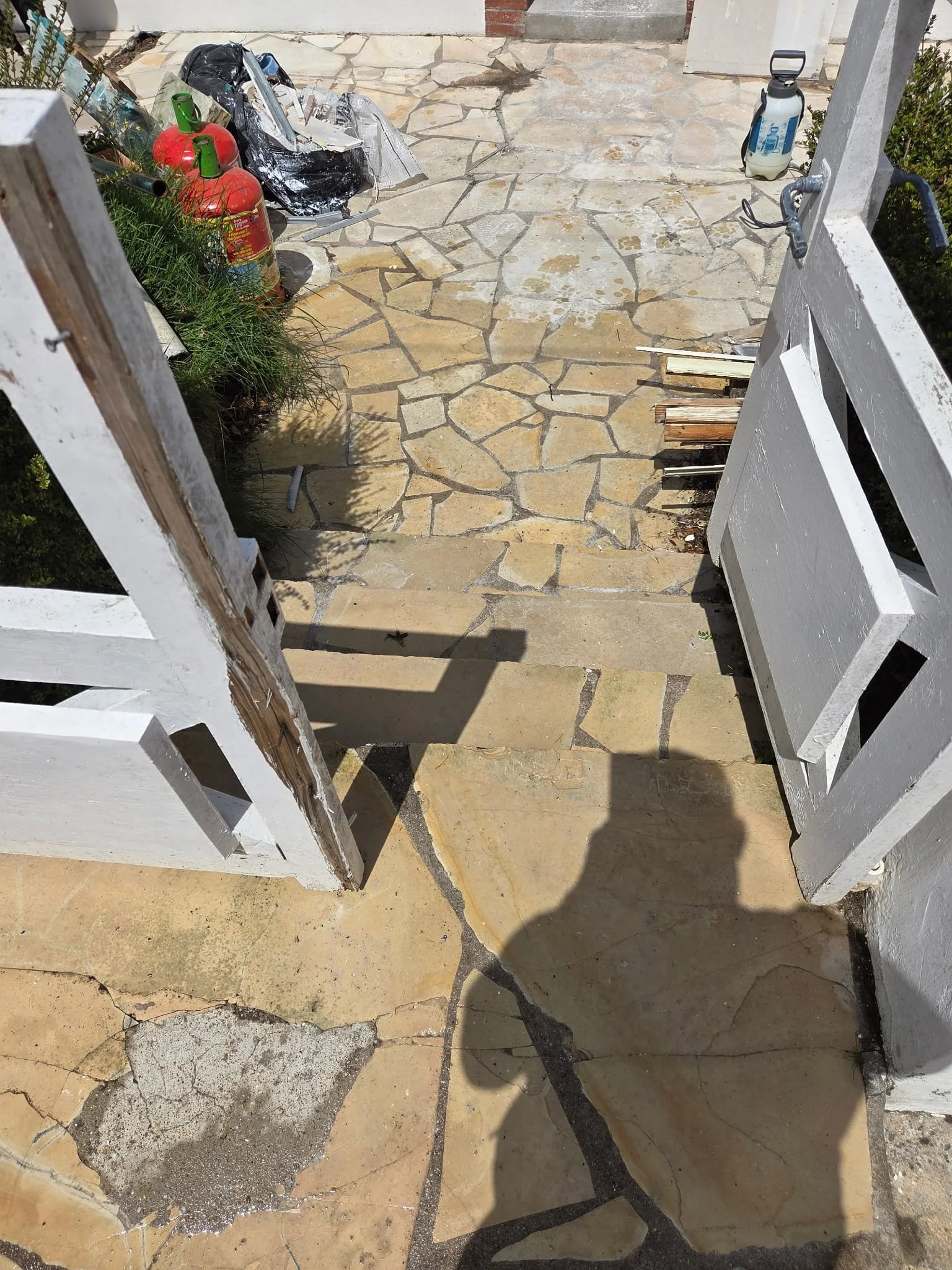 Une véranda en cours de construction ou de rénovation avec un sol en pierre, des outils, des bouteilles de propane, un pulvérisateur d'eau, des planches de bois et des débris.
