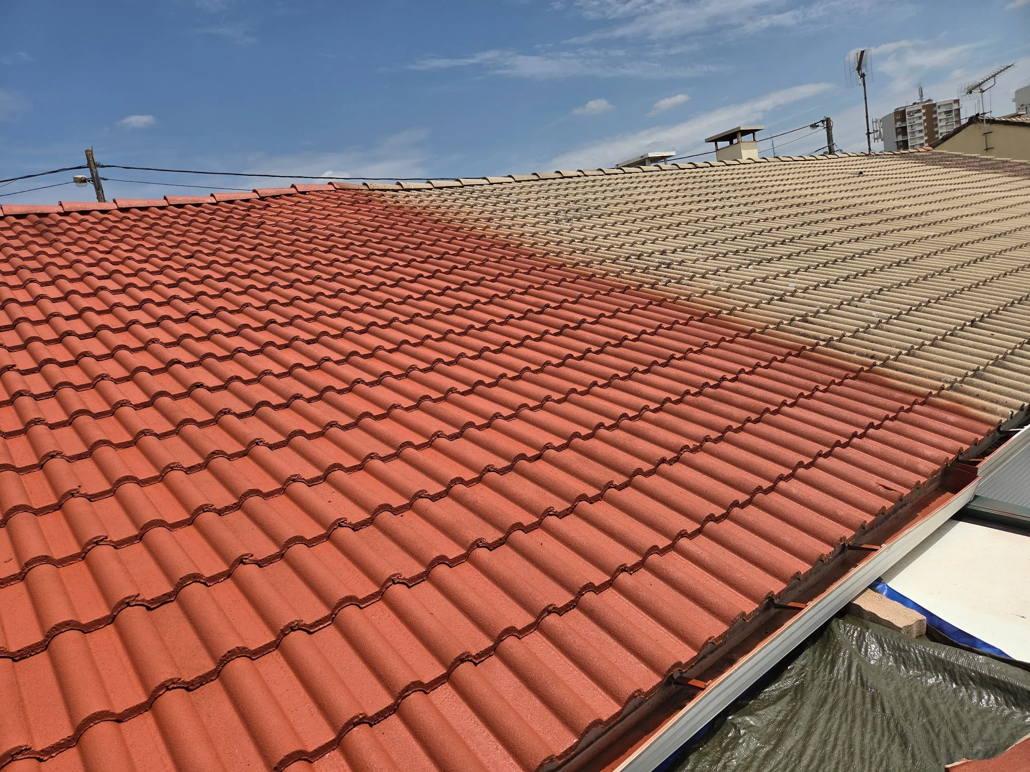 Toit en tuiles rouges et beige, avec quelques antennes et câbles électriques, sous un ciel bleu.