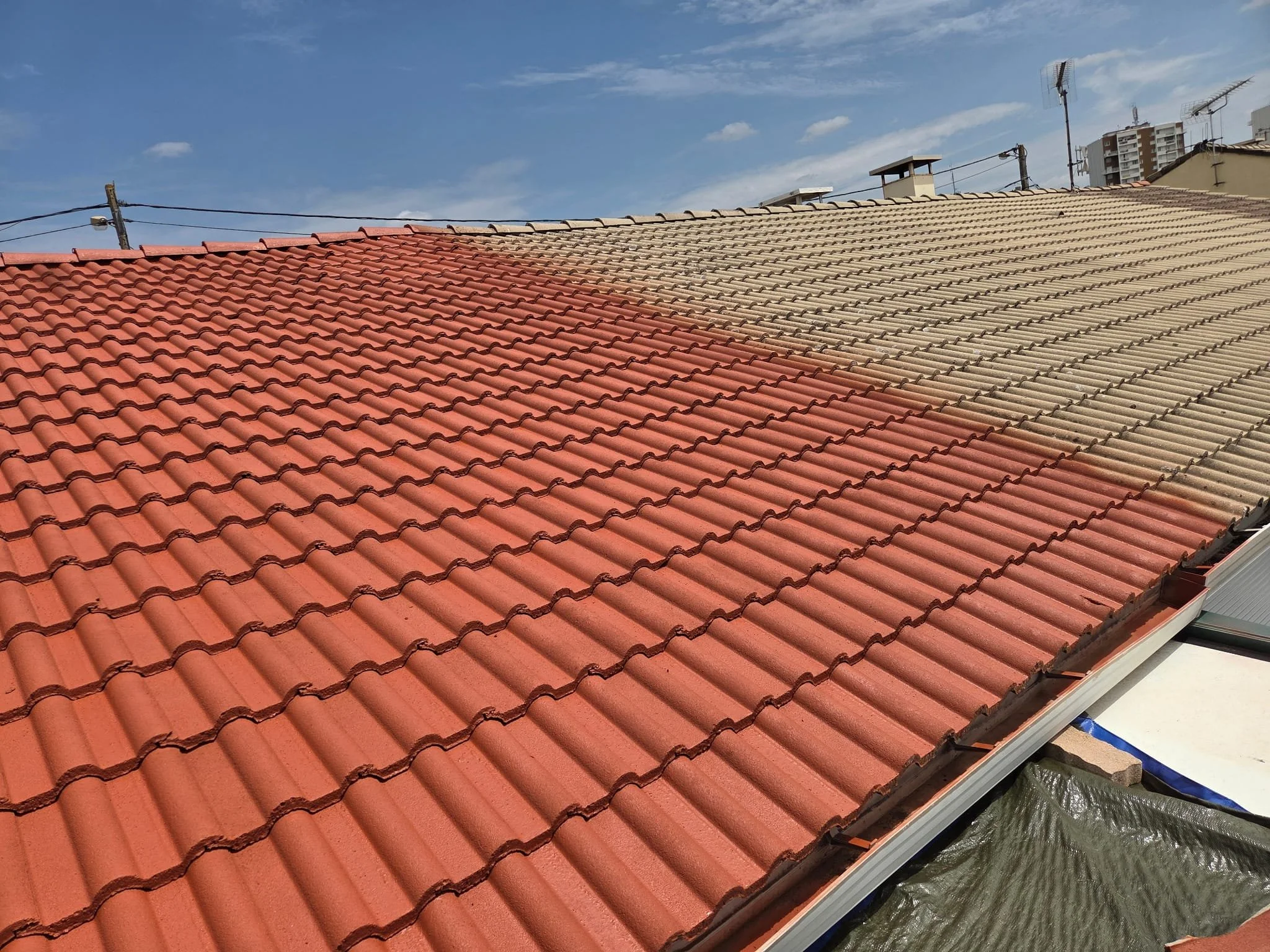 Toit en tuiles rouges et beige avec plusieurs cheminées et antennes, sous un ciel bleu avec quelques nuages.