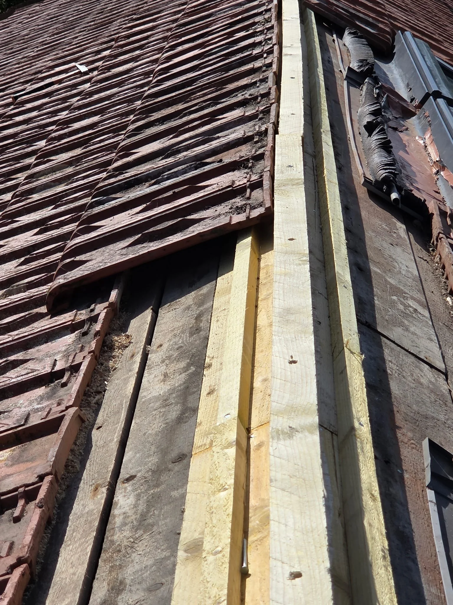 Travaux de construction de toiture avec des tuiles en terre cuite, des planches en bois et des outils pour la pose.