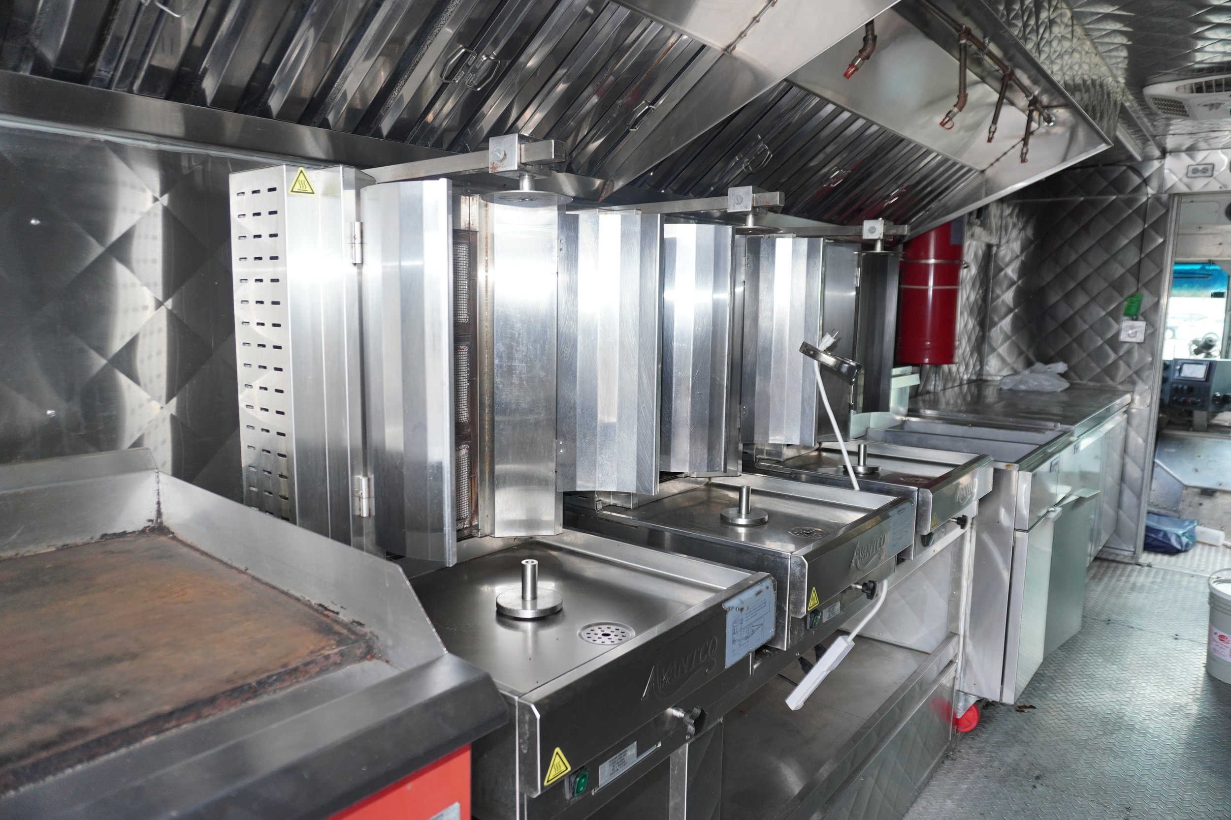 A row of commercial deep fryers in a restaurant kitchen made of stainless steel, with control knobs and some piping above.