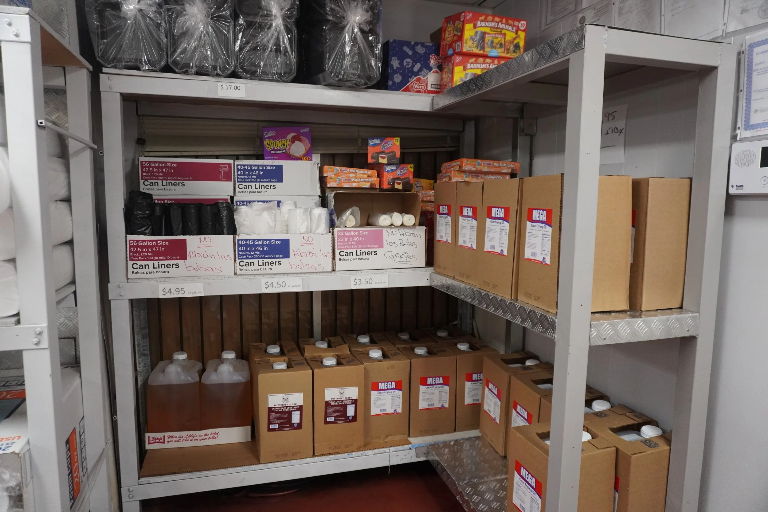 Shelves stocked with various boxes and bottles, including trash bags, cooking oil, and snack boxes, in a storage or warehouse area.