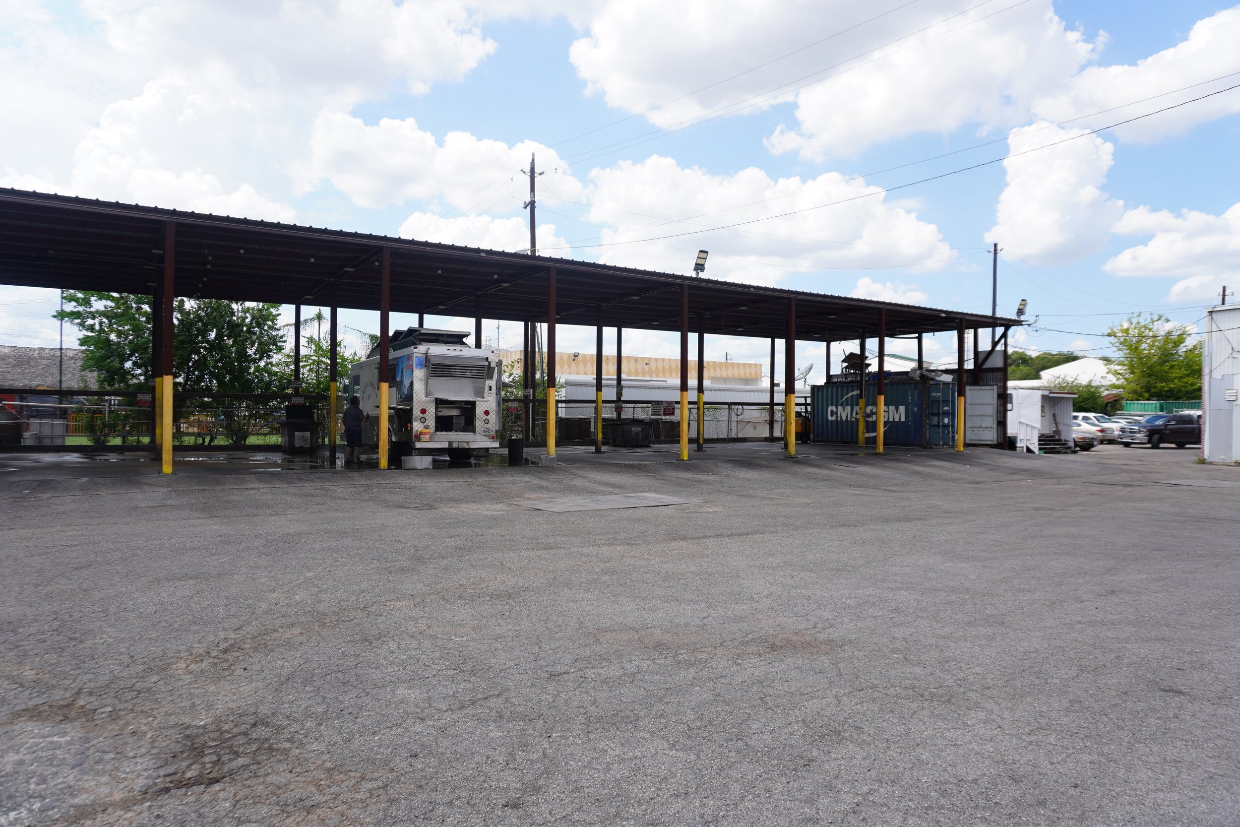 Empty parking lot with covered area, a food truck, and parked cars under a partly cloudy sky.