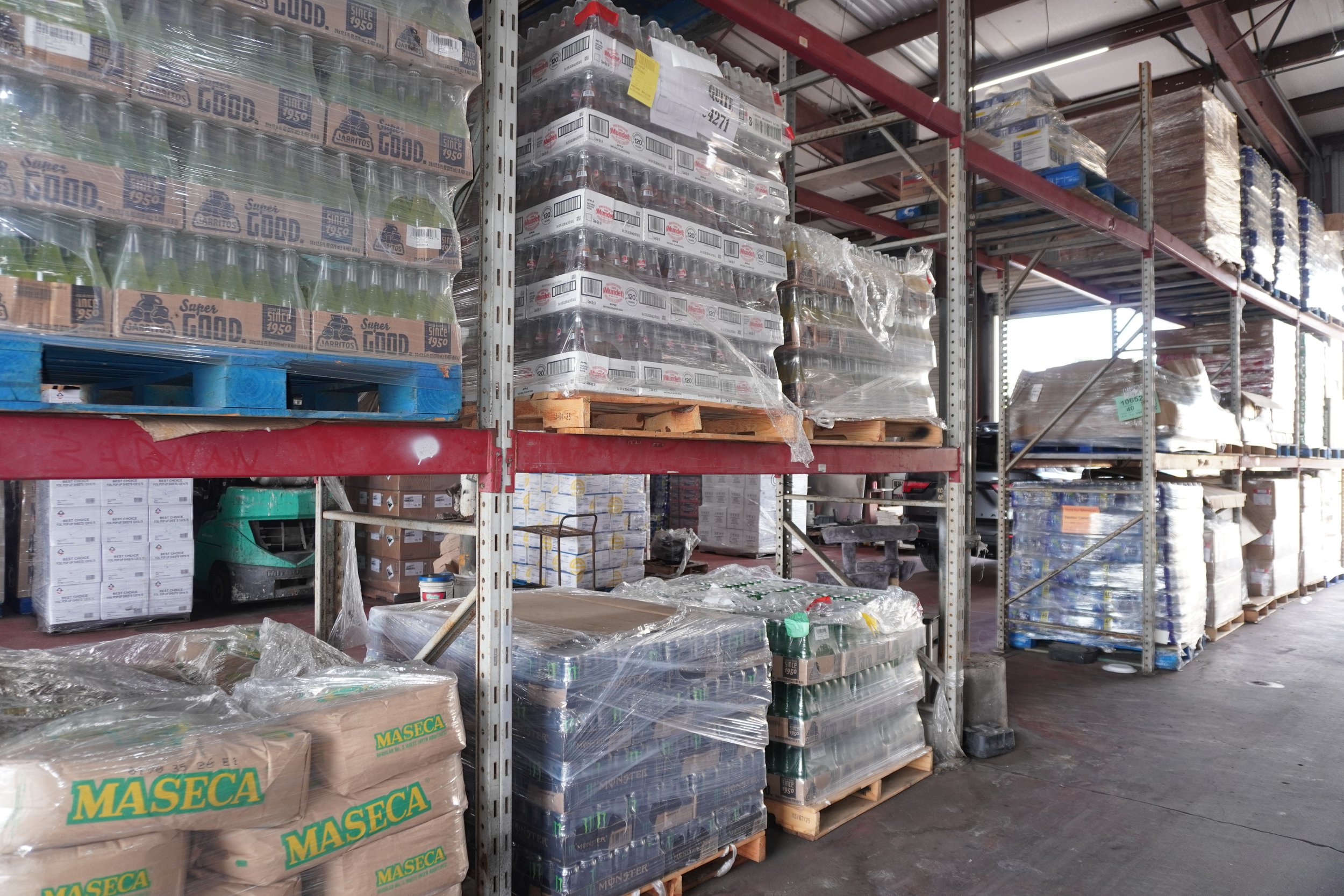 Shelves in a warehouse stocked with bottled beverages and other goods, with some items wrapped in plastic for storage or transport.