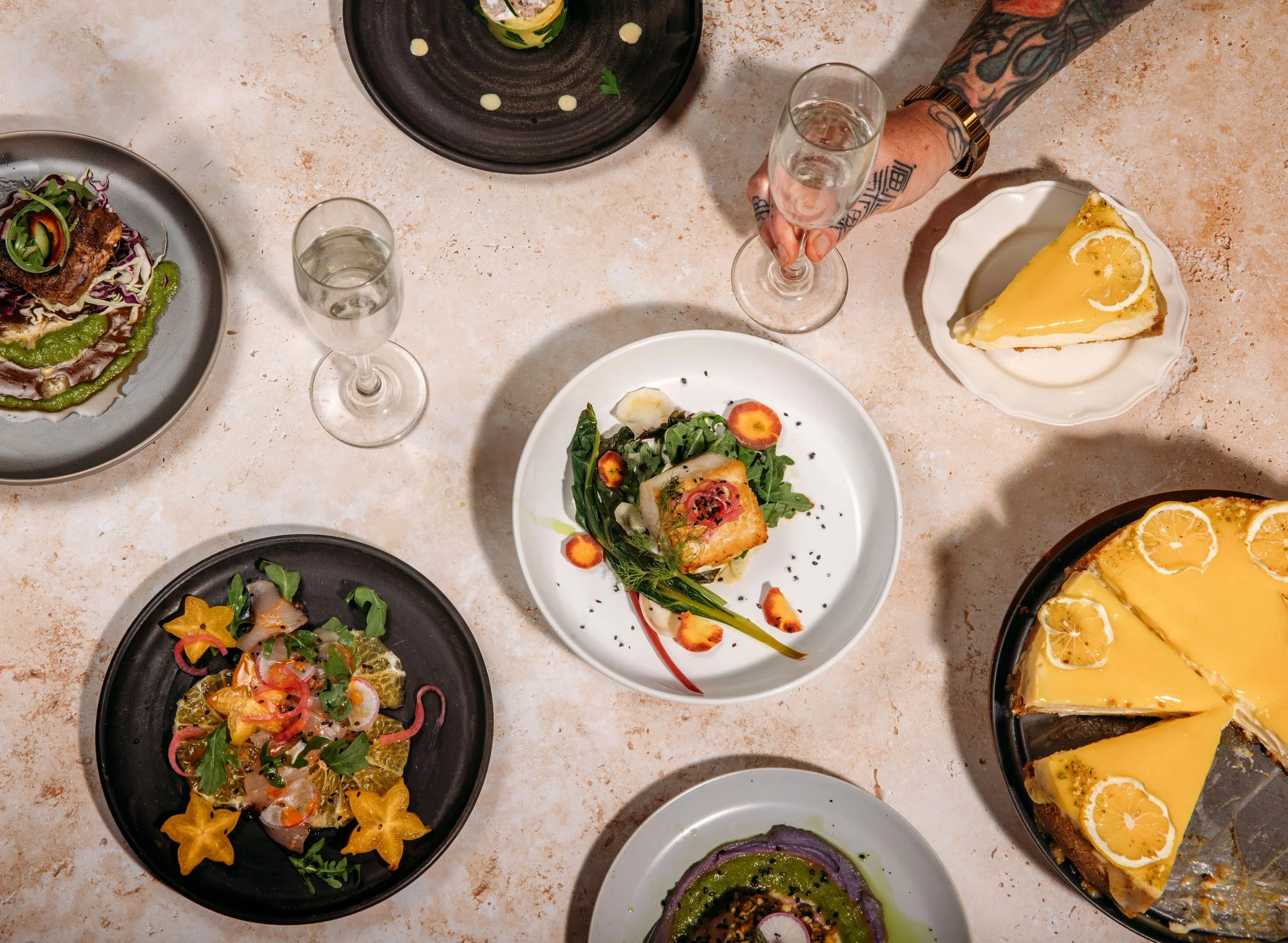 Assorted dishes on a table including a slice of lemon cheesecake, salads, and various main courses with garnishes.