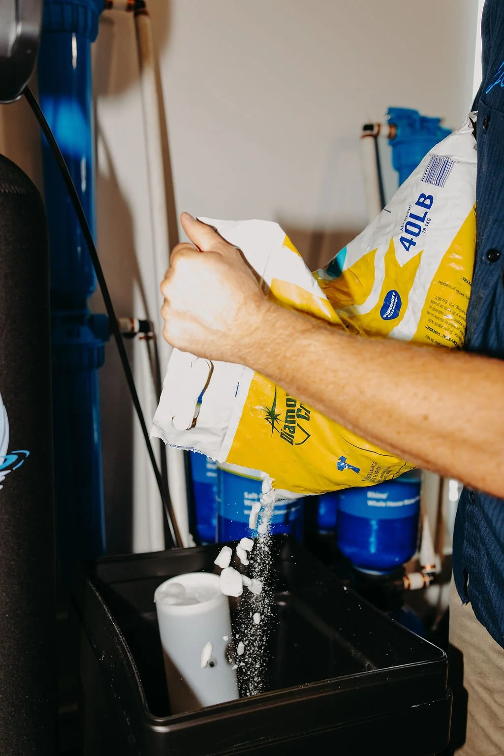 CLR WTR technician pouring salt into a water softener brine tank