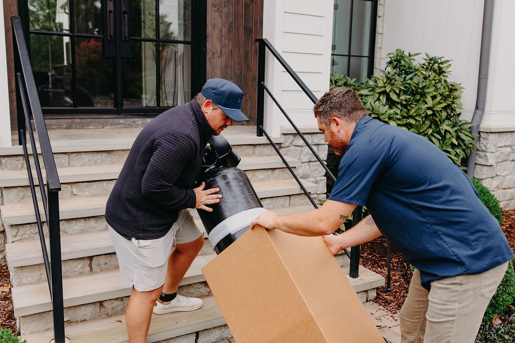 Jon and Jared of CLR WTR Solutions bringing water treatment equipment up a home's porch stairs on install day