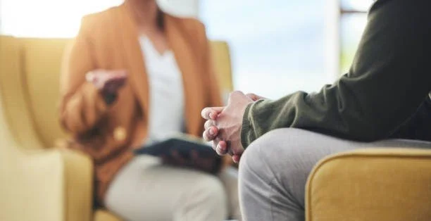 People having a conversation in a waiting room, sitting on yellow chairs.