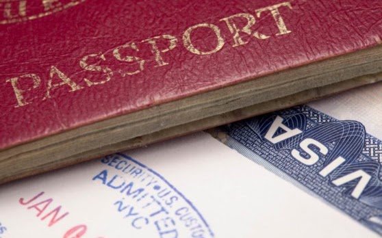 A red passport with gold lettering placed above a US visa on a white surface.