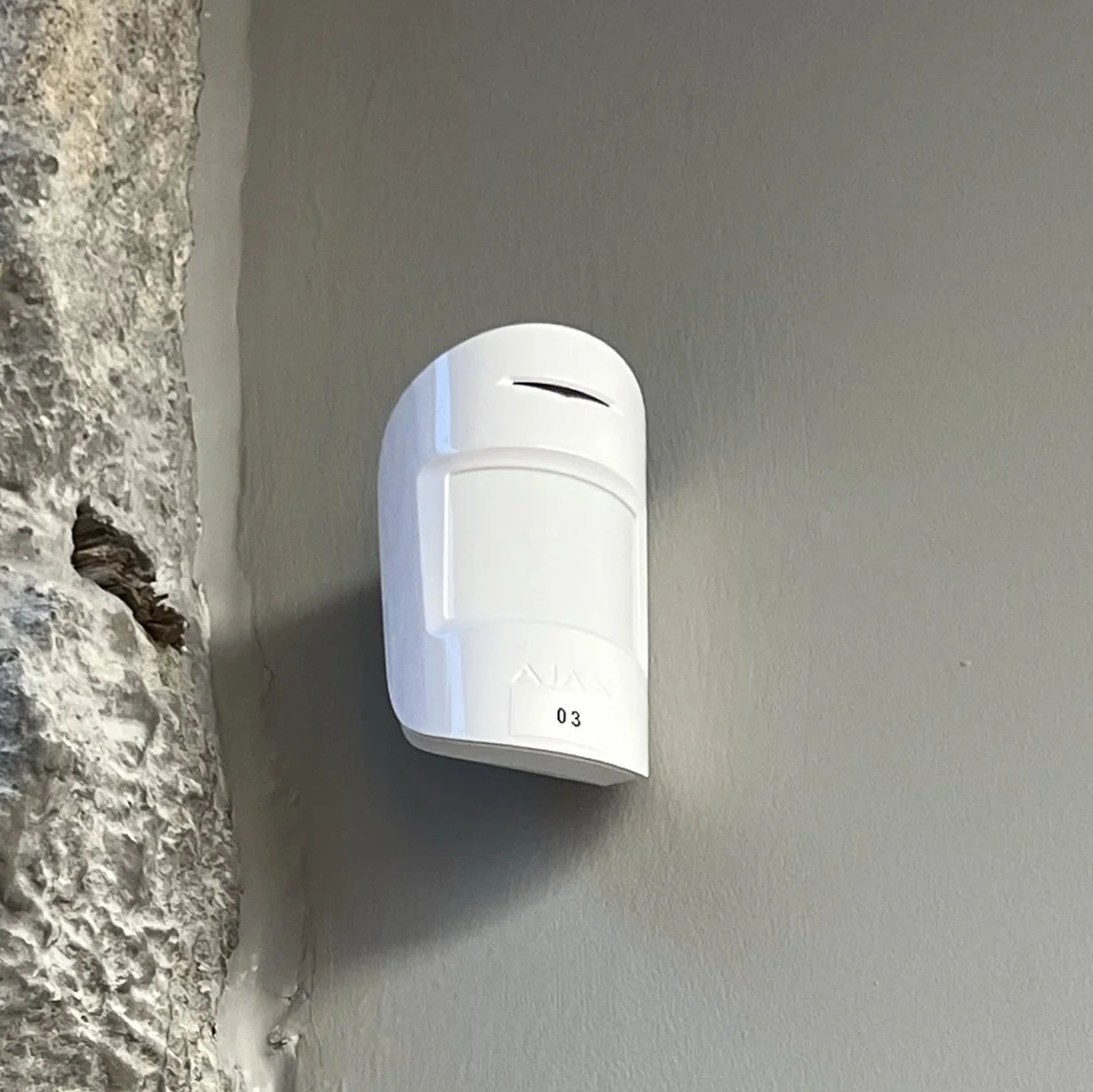En hvid brandalarm placeret i et hjørne mellem en beton og en væg af sten.