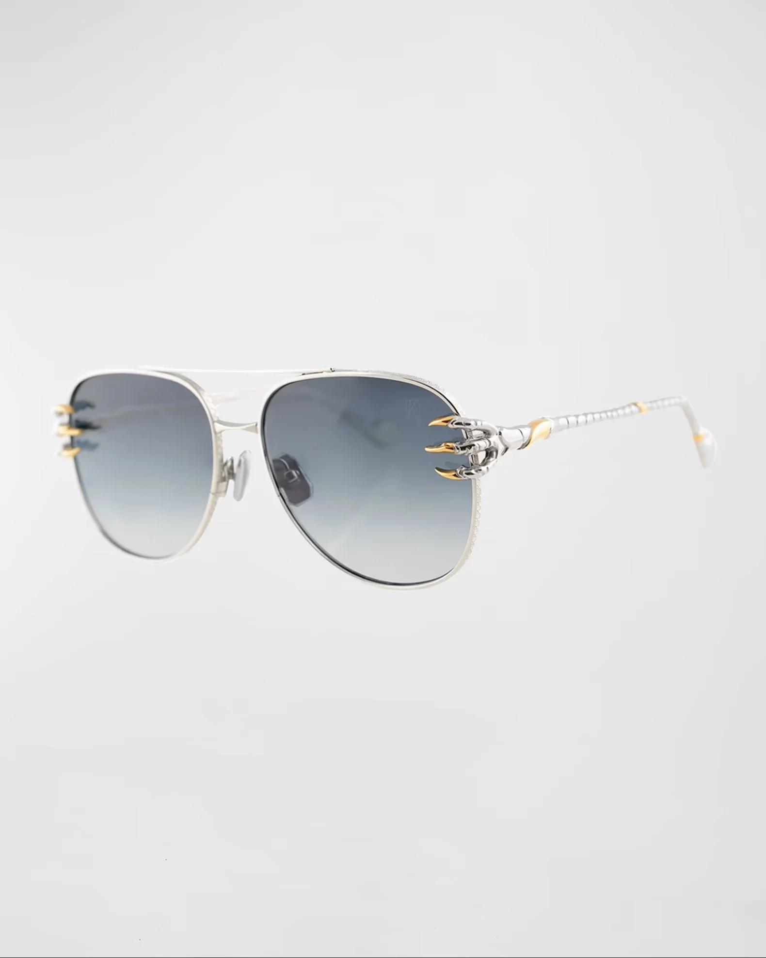 Silver sunglasses with dark tinted lenses and decorative pointed gold accents above the temples, placed on a plain gray background.