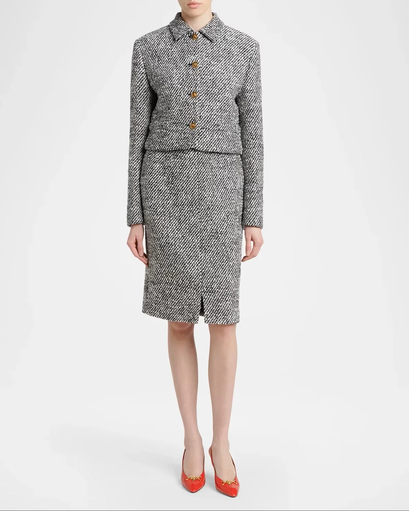 A woman is wearing a coordinated black and white herringbone patterned suit with a matching skirt and blazer with gold buttons, and red high heel shoes with gold embellishments.