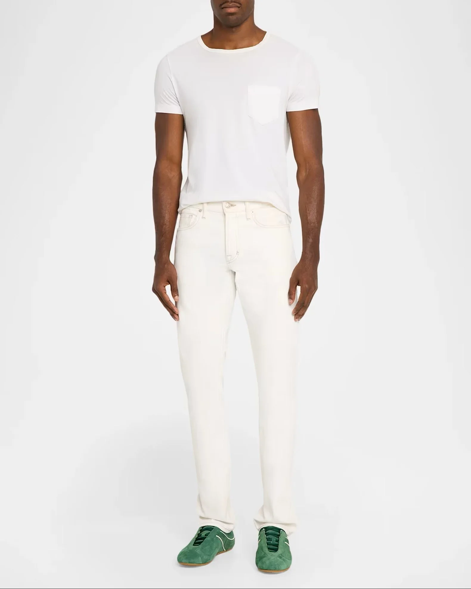A person dressed in white pants, white t-shirt, green sneakers, standing against a plain gray background.
