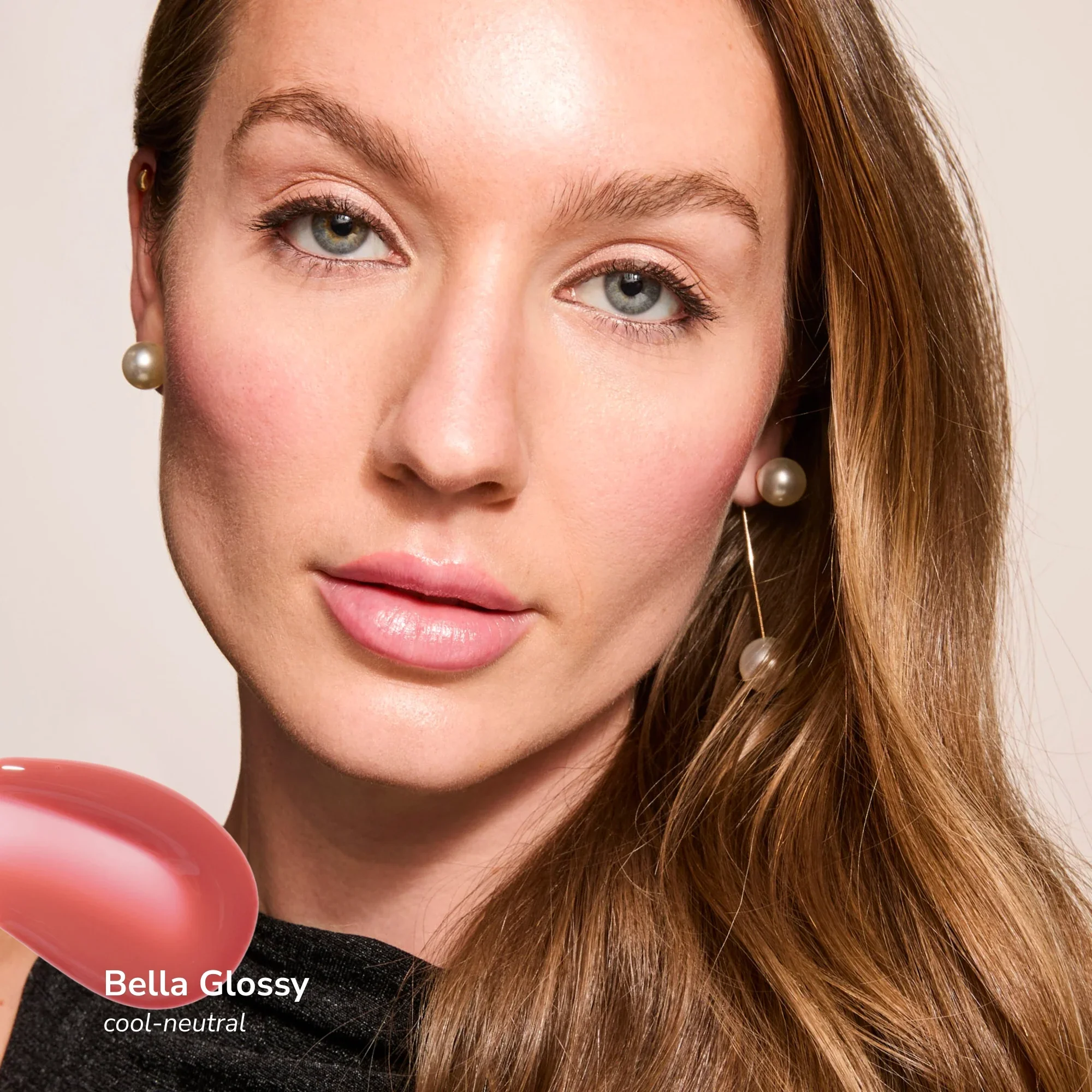 Close-up of a woman's face with fair skin, green eyes, freckles, and long light brown hair. She is wearing pearl earrings. Part of a pink heart shape and the text 'Bella Glossy cool-neutral' is visible at the bottom.