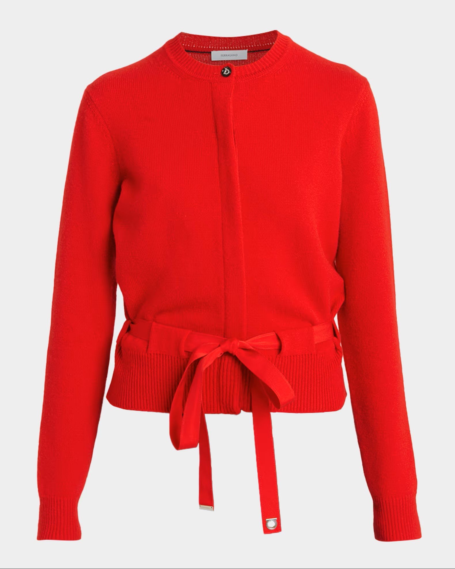 A bright red cardigan sweater with a ribbon tie detail at the waist and a small logo tag near the bottom of the ribbon.