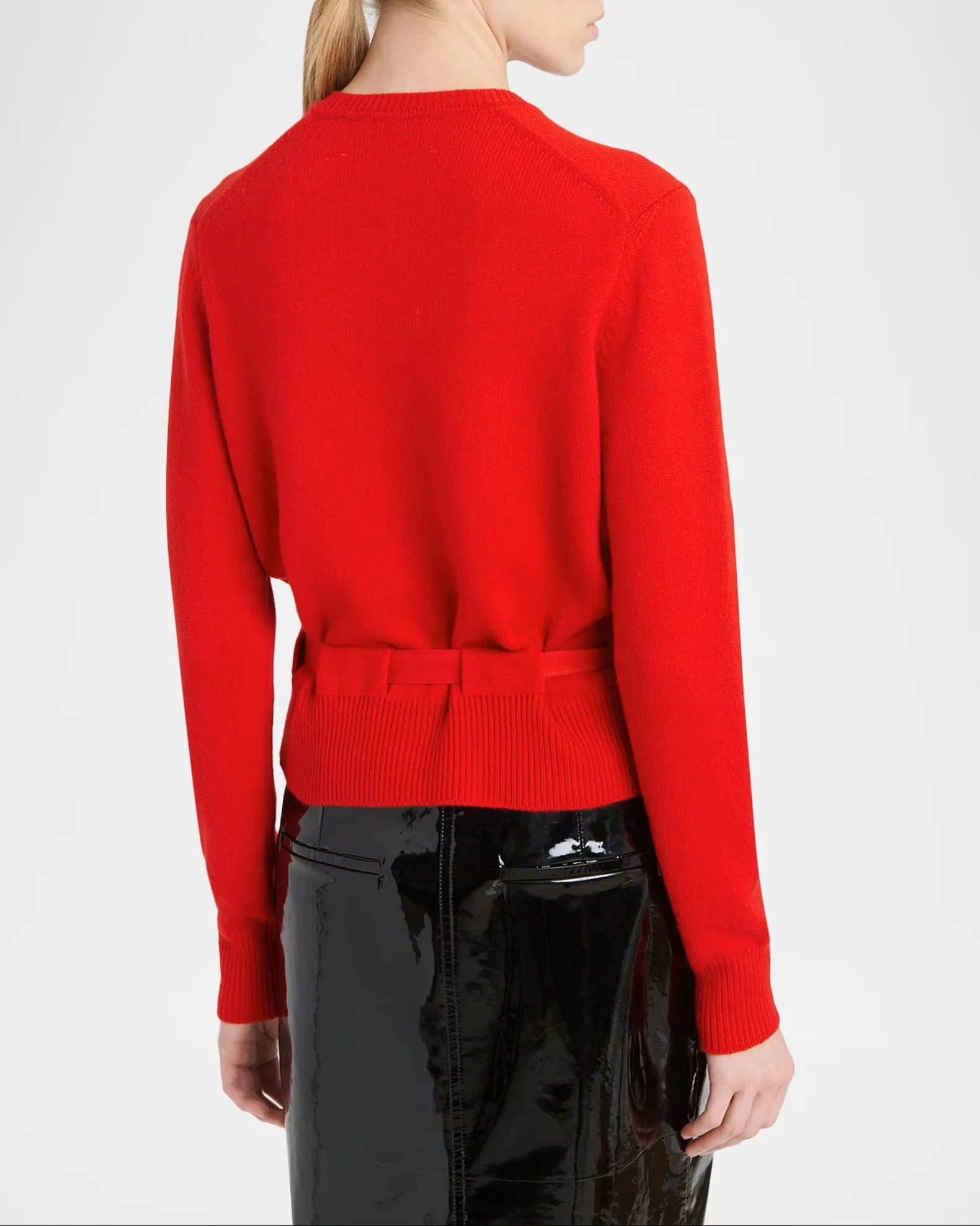 Back view of a person wearing a long-sleeved red sweater and high-gloss black patent leather skirt.