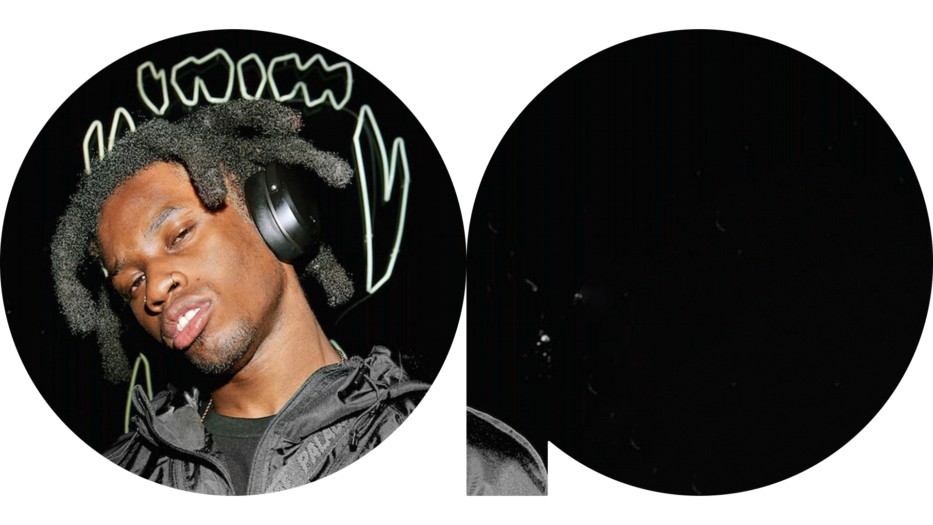 A young man with dreadlocks wearing headphones and a black jacket, with a neon sign in the background.