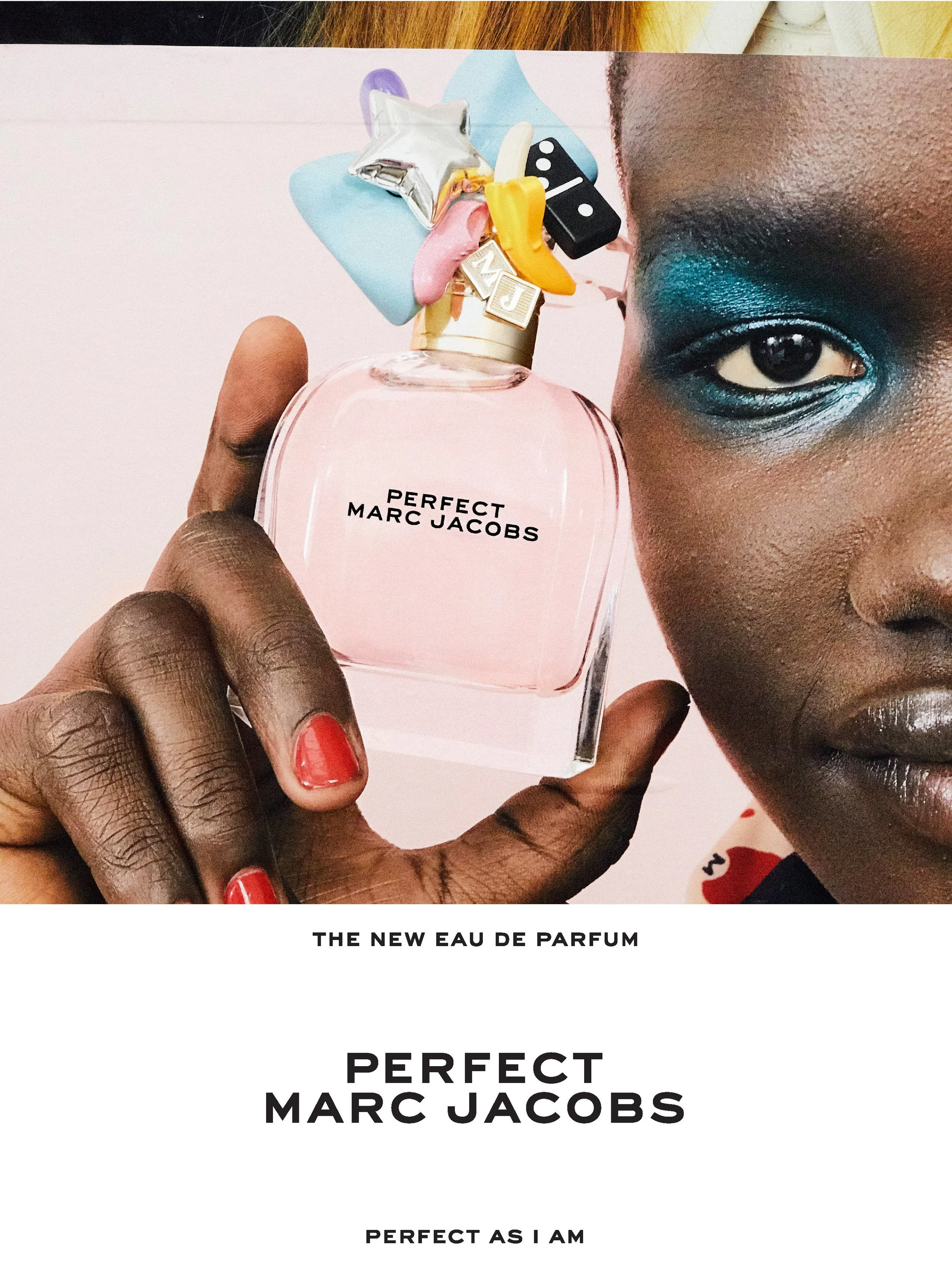 A person with dark skin and vibrant blue eye makeup holding a pink bottle of Marc Jacobs perfume labeled "Perfect" close to their face. The person's nails are painted red. Footage highlights the perfume bottle, part of the person's face and eye makeu