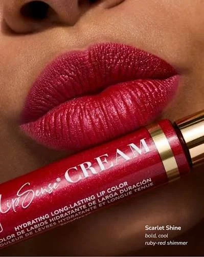 Close-up of lips with bold, ruby-red shimmer lipstick, holding a tube of LipSense lip color labeled 'Sense CREAM' in ruby-red.