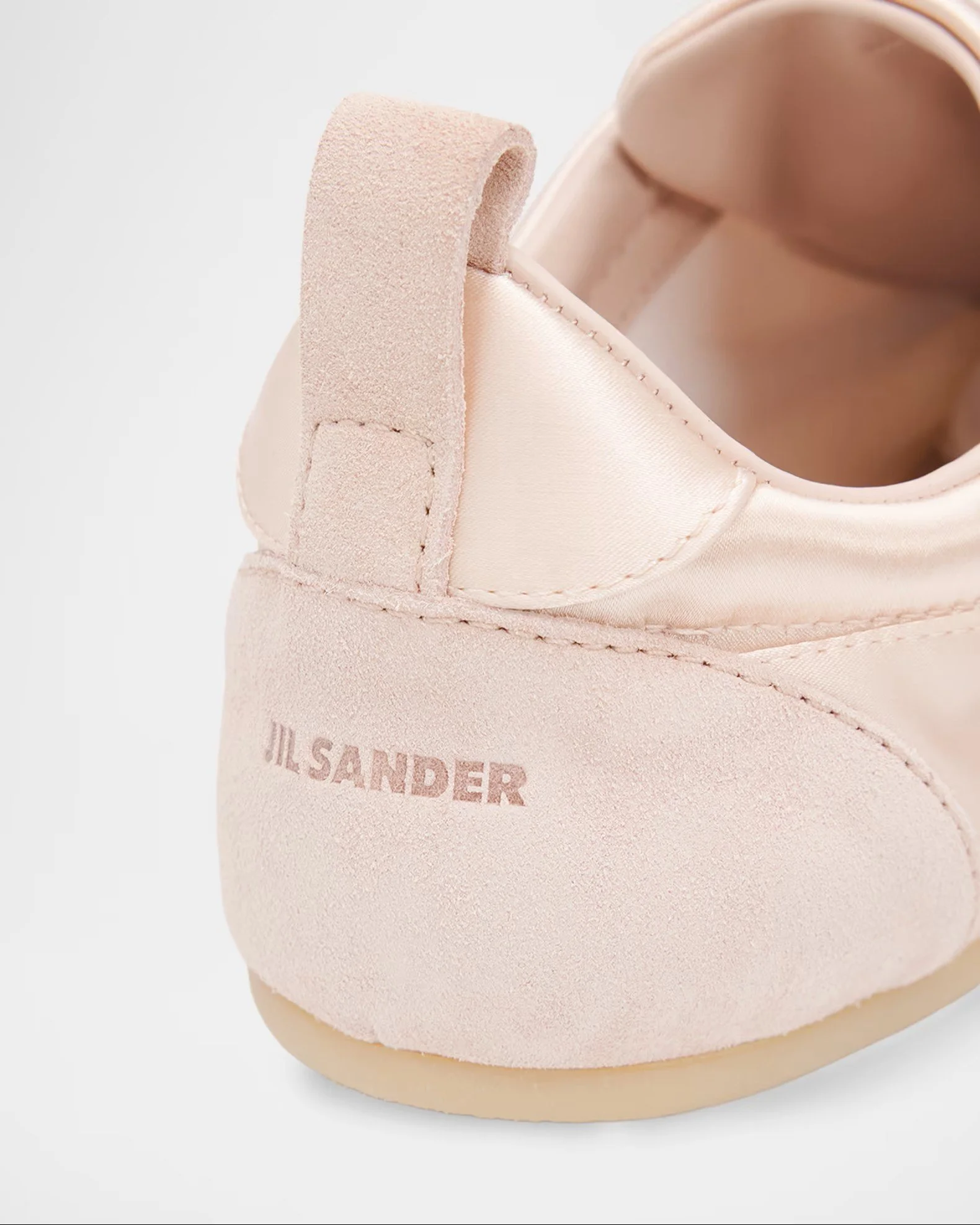 Close-up of a light pink ballet flat shoe, showing the textured velcro strap and stitching on the side, with a soft cream-colored upper and the brand name partially visible.