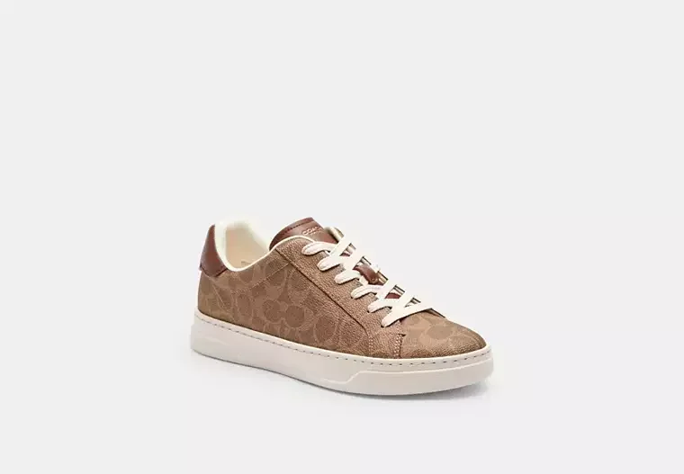 Brown designer sneaker with white sole and laces, against a plain background.