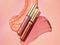 Two tubes of lipstick with pink and nude lipstick smears on a pink background.