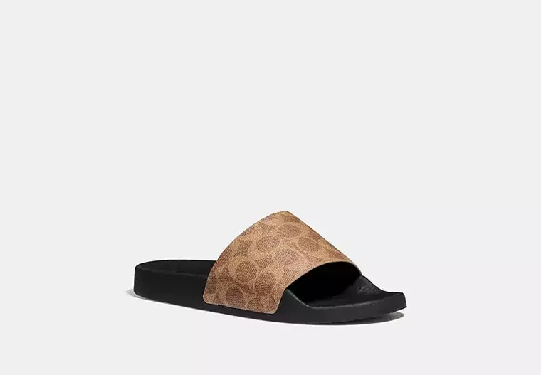A single slide sandal with a black sole and a tan strap featuring a pattern, placed on a plain gray background.
