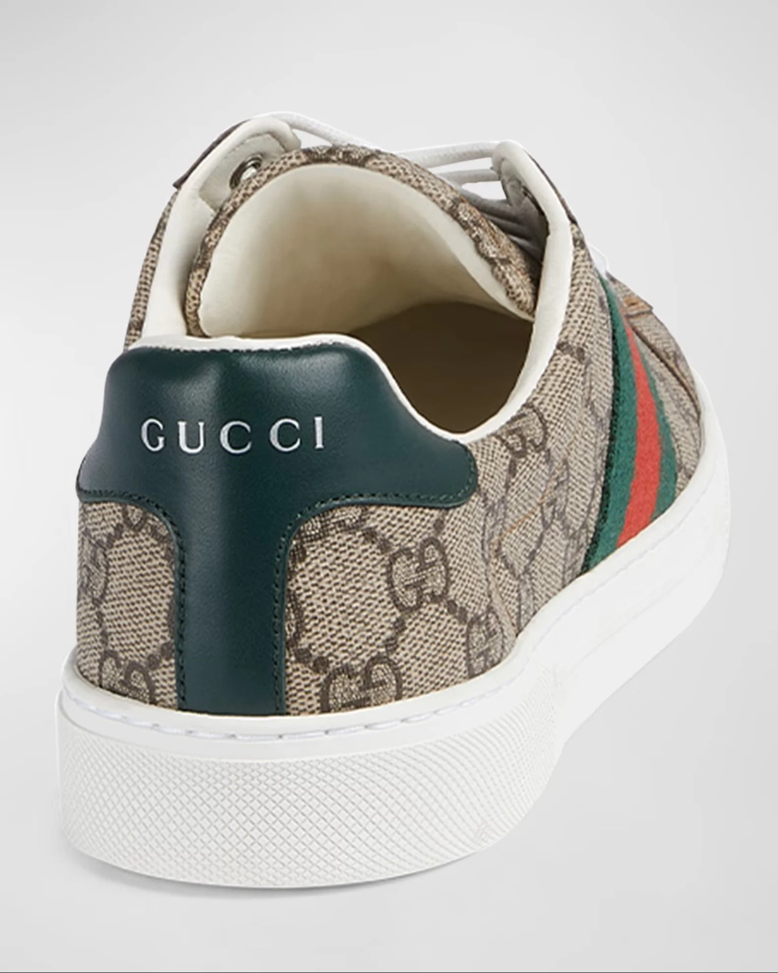 A luxury designer sneaker with a beige and brown monogram pattern, black leather heel tab with white text 'GUCCI', green and red striped webbing on the sides, and white rubber sole.