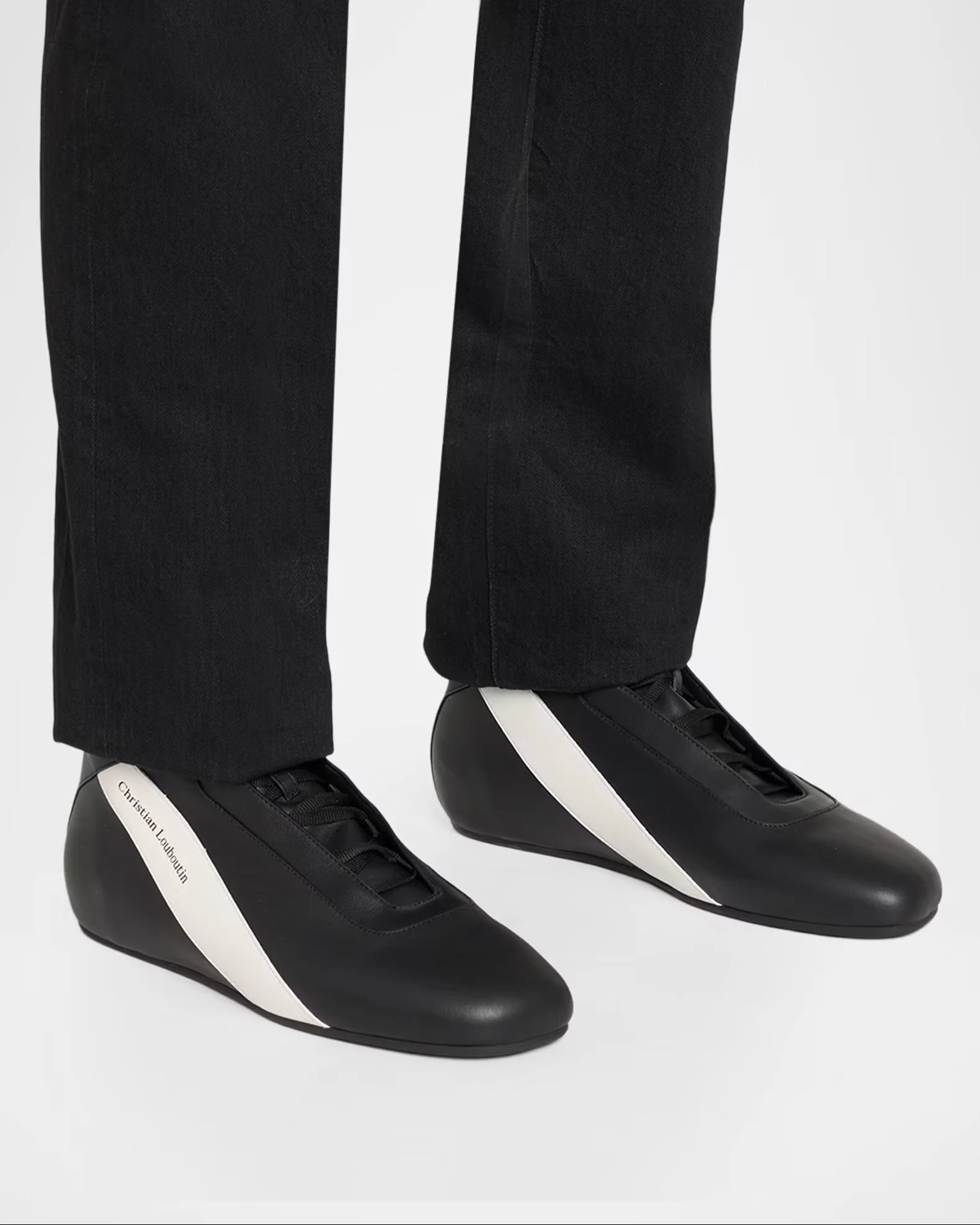 Close-up of black leather and white sneakers with the name 'Christian Louboutin' written on the side, paired with black pants.