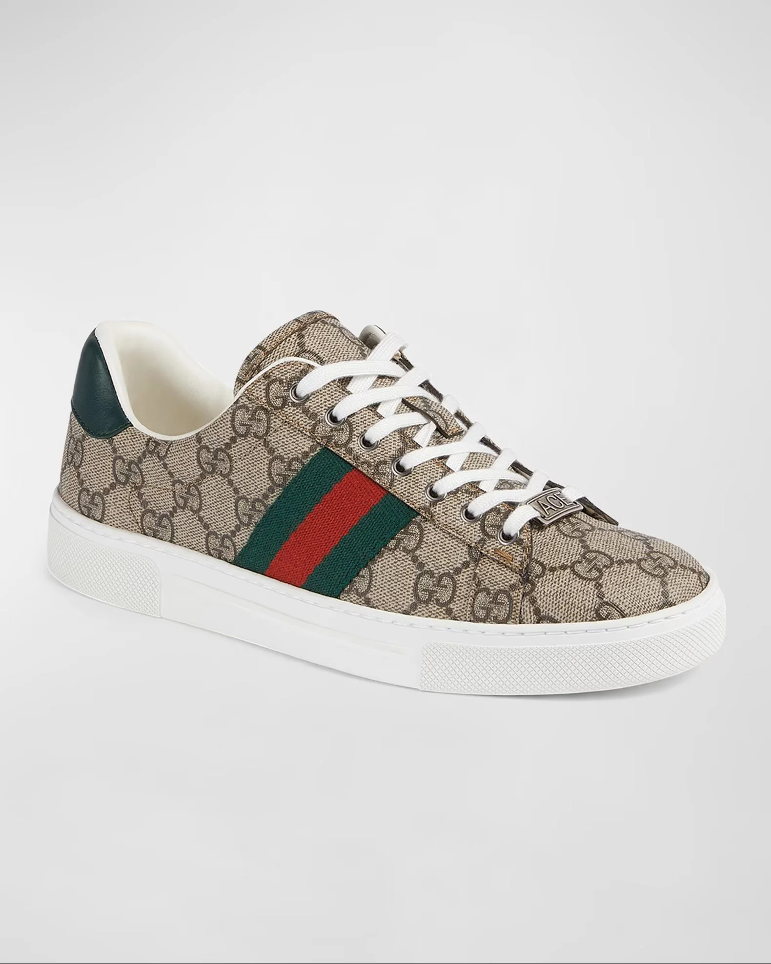 A designer sneaker featuring a beige monogram canvas with Gucci's GG pattern and green and red stripes on the side, against a plain gray background.