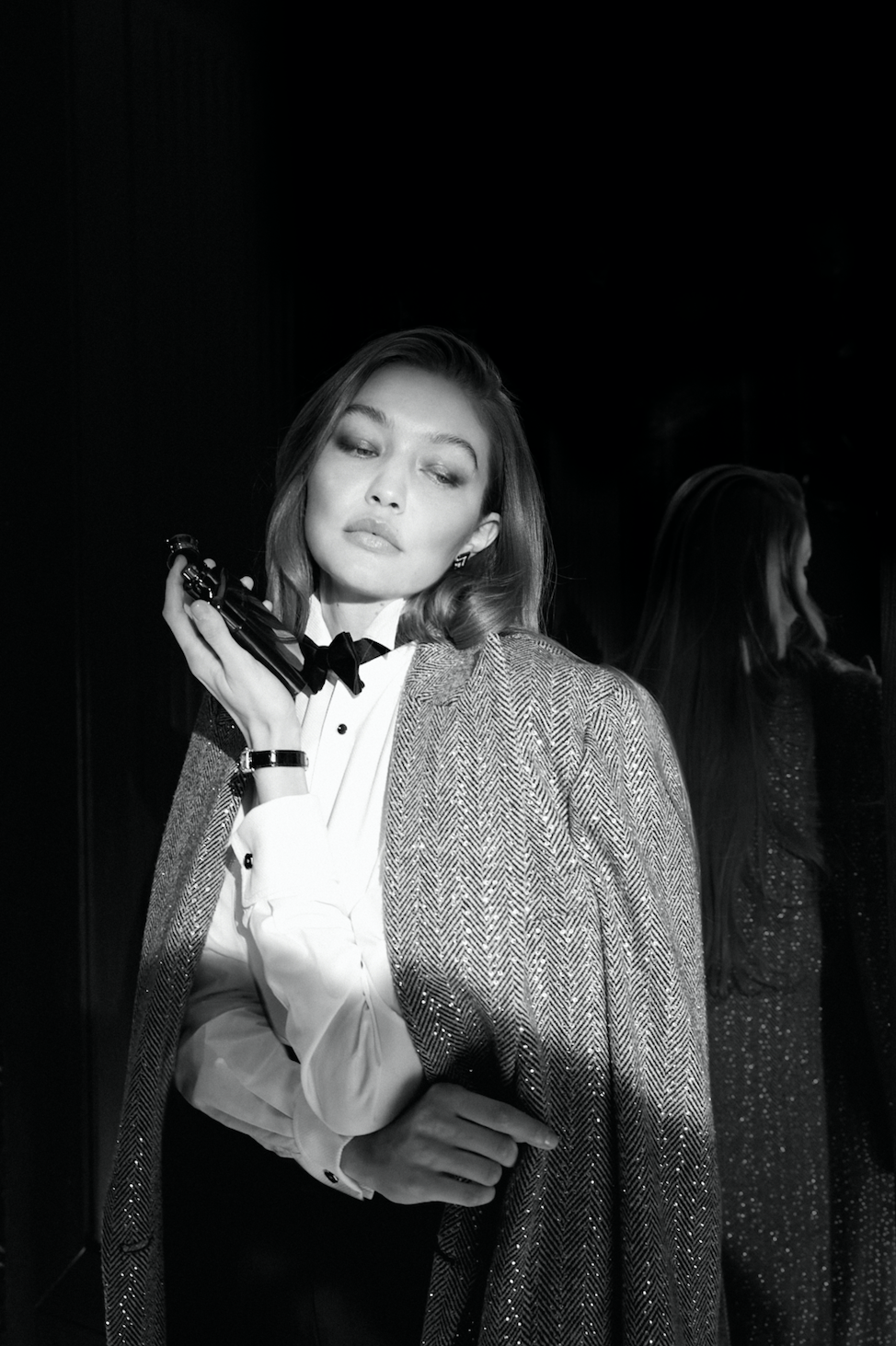 Black-and-white photo of a woman in a tuxedo with a cape, holding a gun to her shoulder, with another woman in the background.