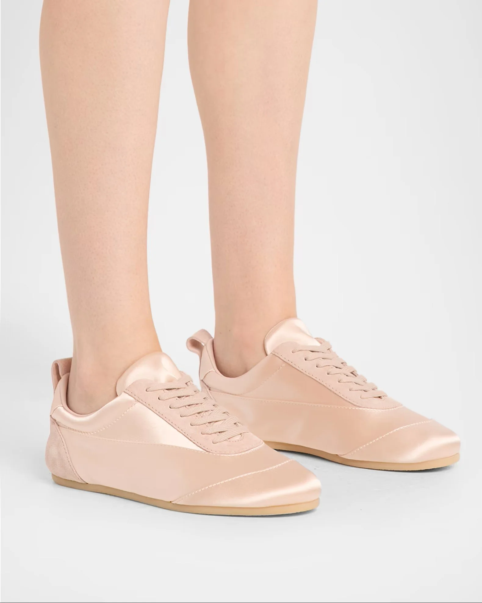 Close-up of a person's feet wearing light pink sneakers with laces, standing on a plain surface.