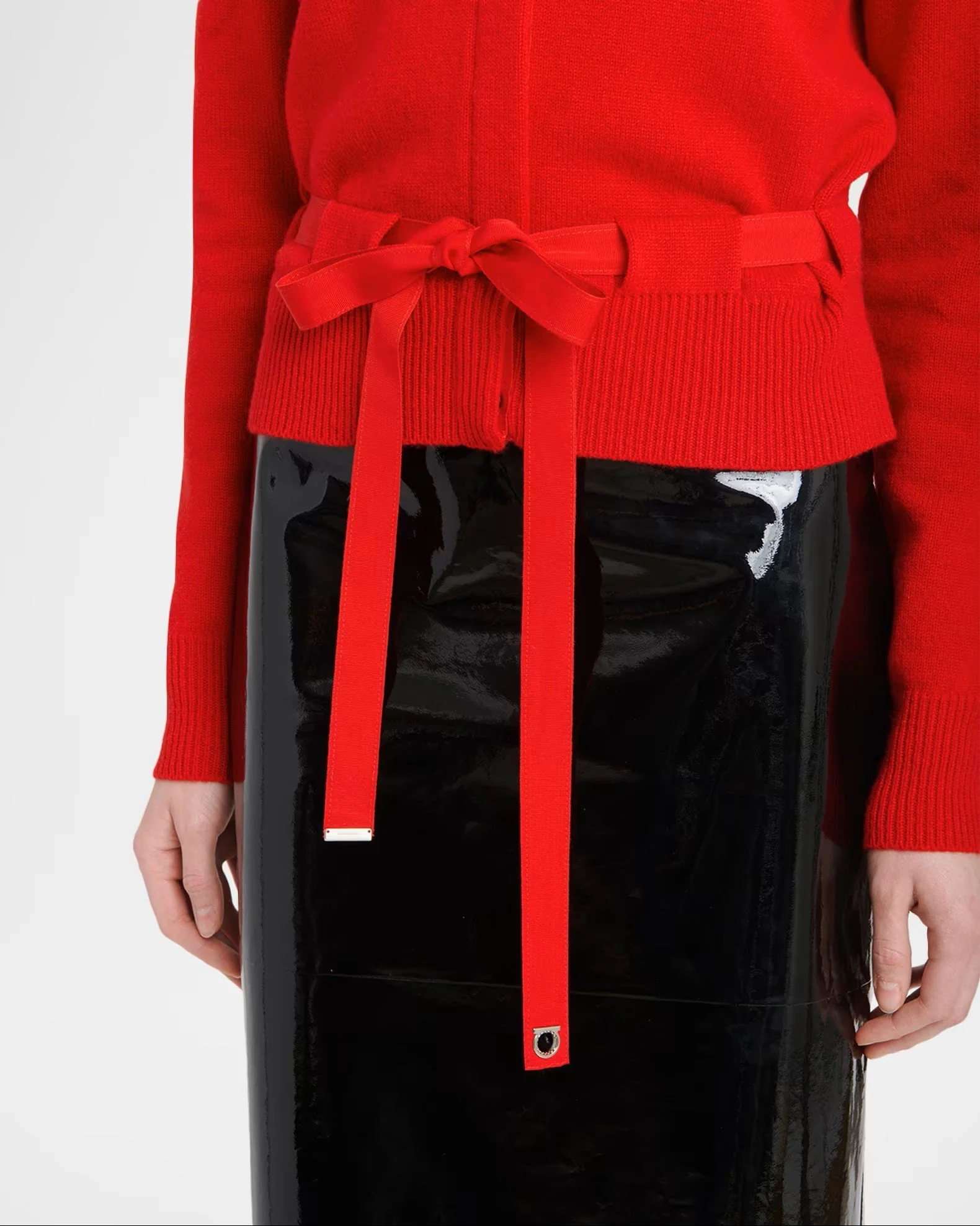 A woman wearing a red jacket with a matching belt, and black shiny pants with white accents, standing against a plain white background.