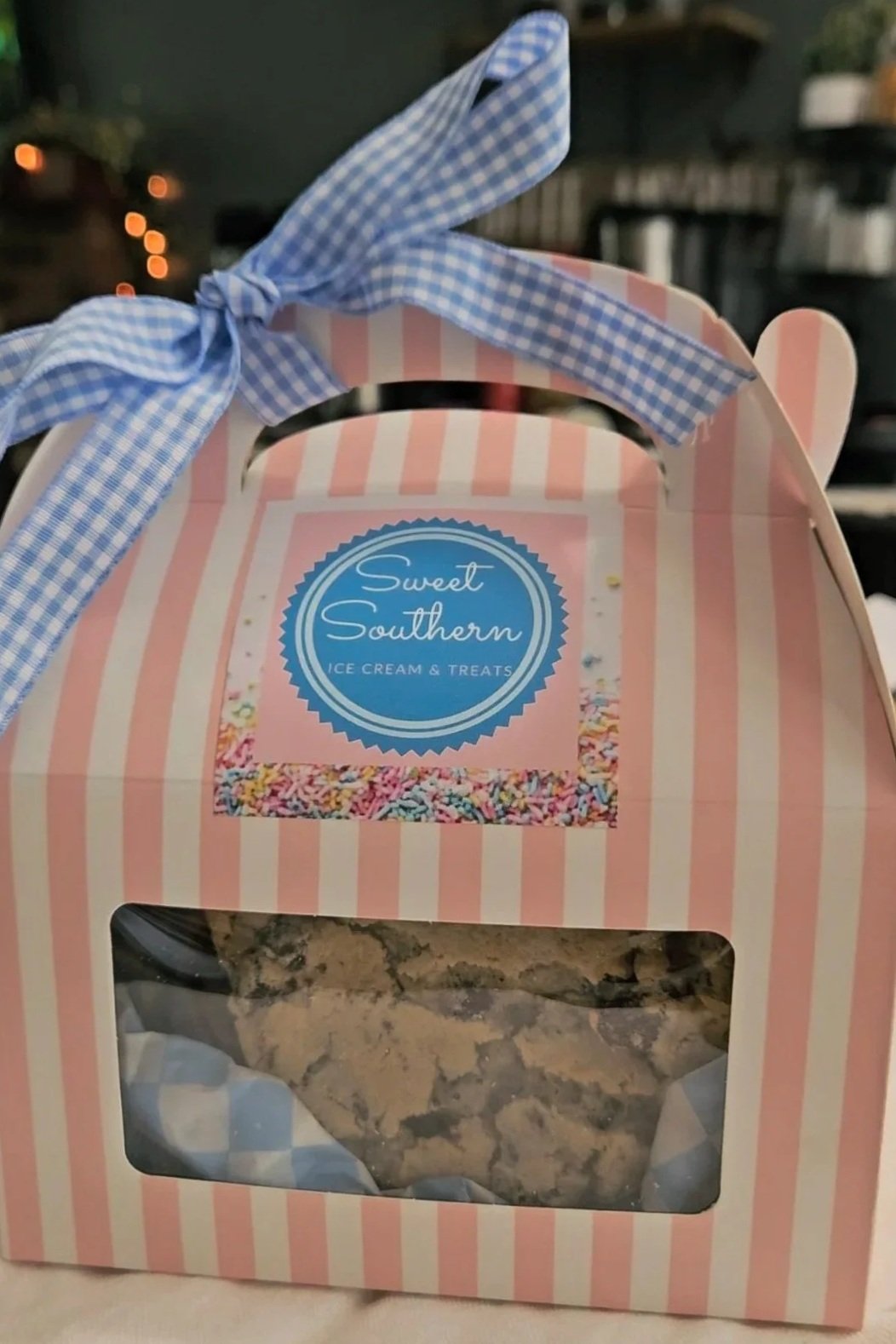 Pink and white striped gift box with a clear window showing cookies inside, topped with a blue gingham ribbon and a label that reads "Sweet Southern Ice Cream & Treats" with colorful sprinkles.