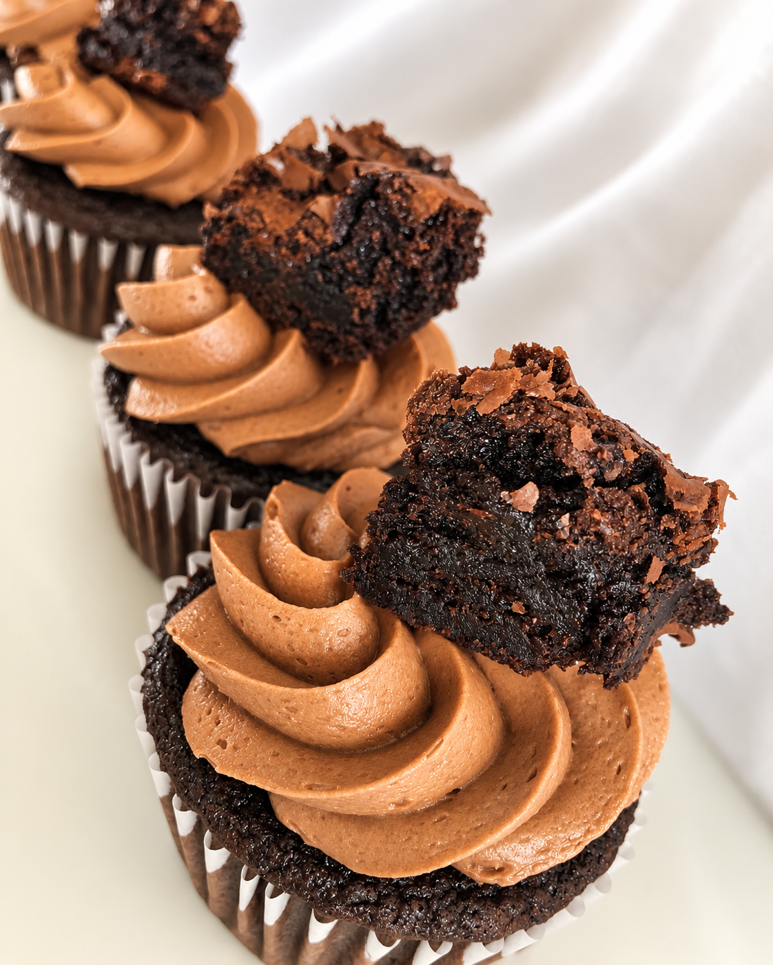 Close-up of three chocolate cupcakes decorated with caramel-flavored frosting and topped with chunks of chocolate brownie.