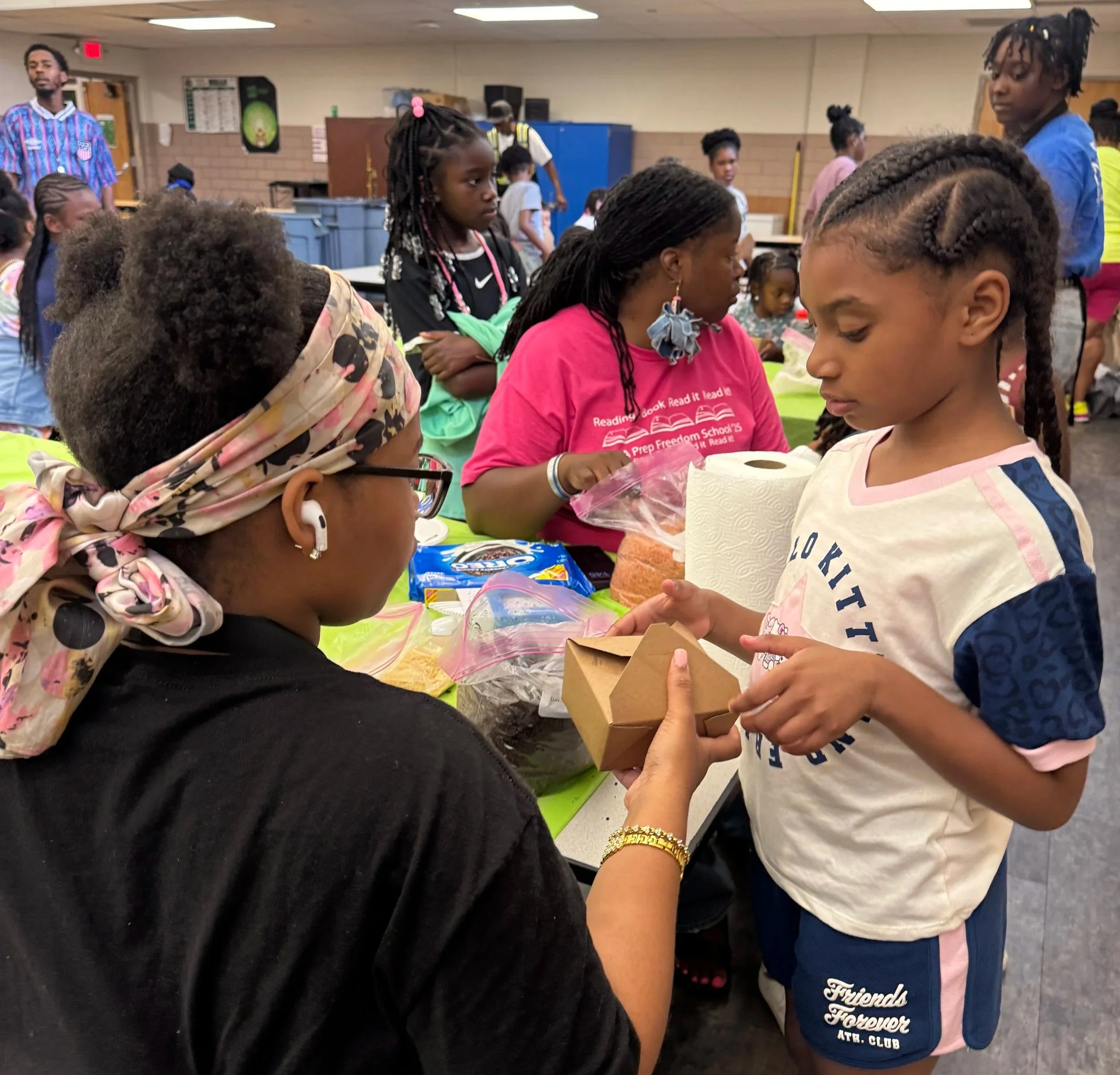 Children and adults gathered indoors around a table with food and drinks during a Sweets by Peeks Hands-on Class.