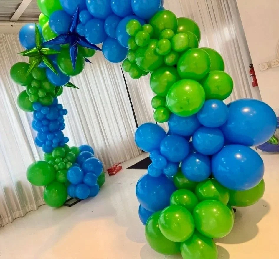 Balloon arch decorated with blue and green balloons, including star-shaped balloons, set against white curtains in an indoor space.