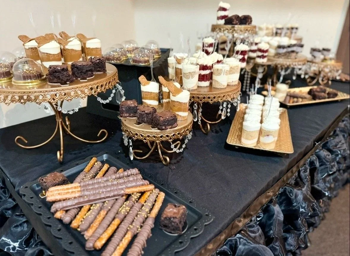 A dessert table with various chocolate and vanilla sweets on gold and black stands, including layered parfaits, brownie bites, and cookies.