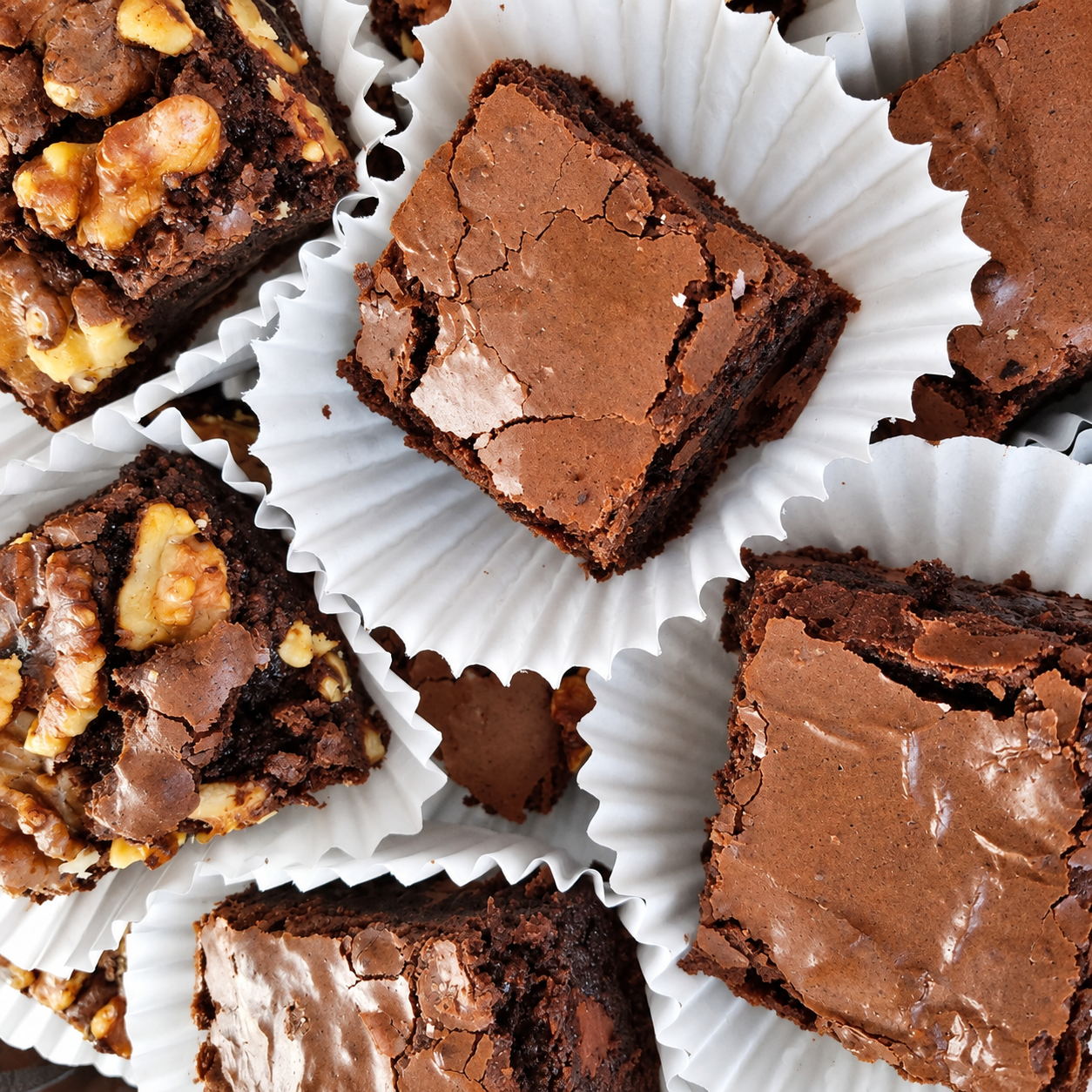 Close-up of assorted brownies in white paper cups, some topped with walnuts.