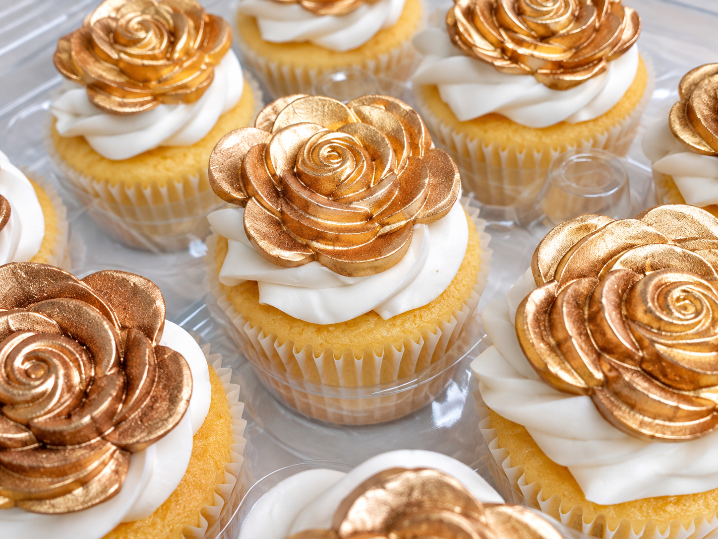 Cupcakes with white frosting topped with sweet gold rose decorations
