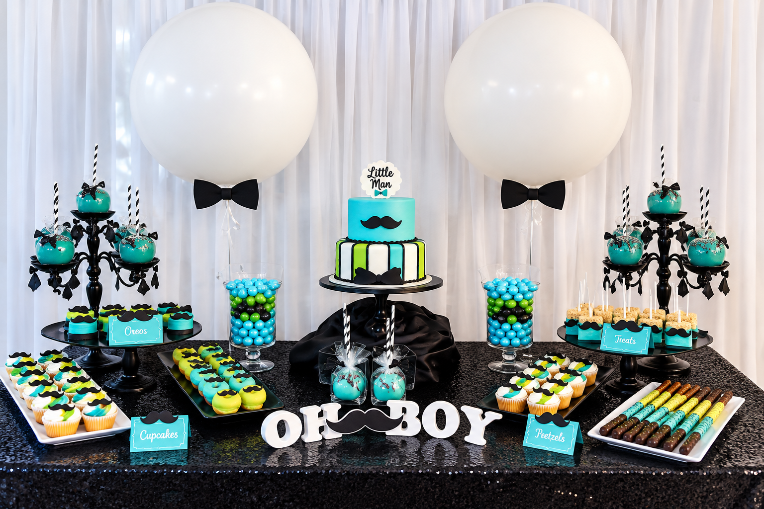 A baby shower dessert table with a black, blue, and green color theme. The table features a two-tiered cake with mustache and bowtie decorations, large white balloons with black bowtie accents, and various cupcakes, cake pops, and treats.