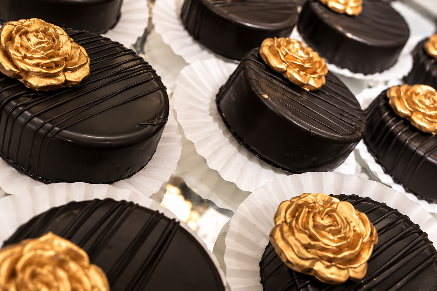 Chocolate covered oreos with gold roses and chocolate stripes, placed on white paper liners.