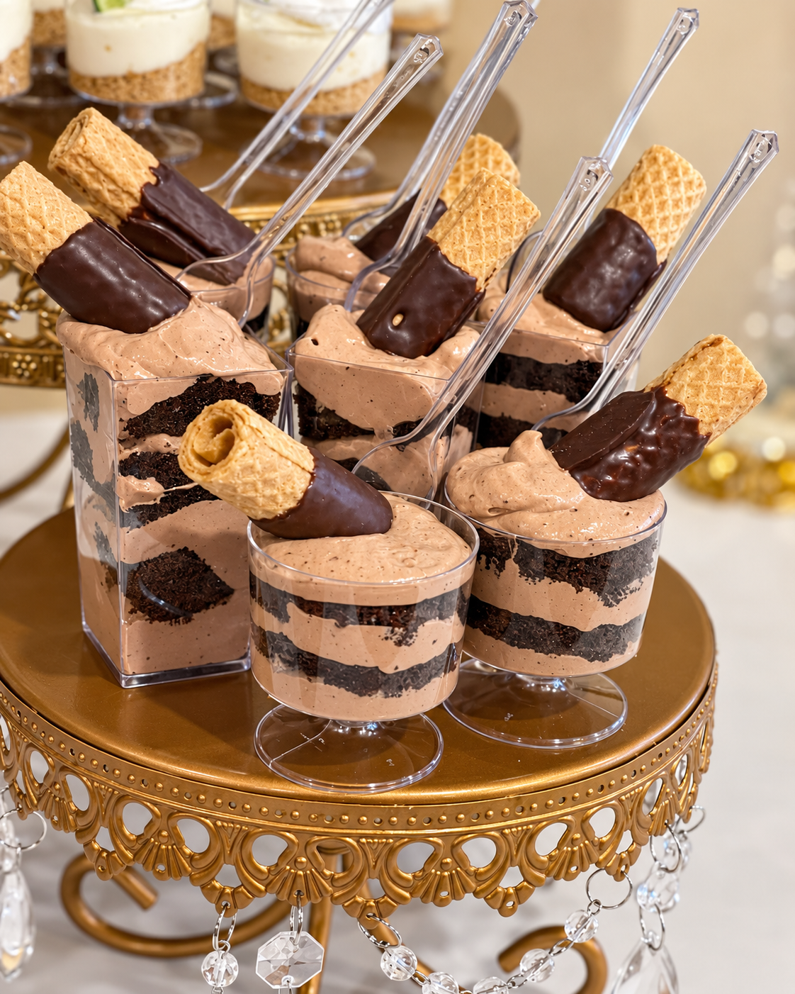 Chocolate mousse dessert cups topped with waffle cookies dipped in chocolate, served on a decorative gold stand.